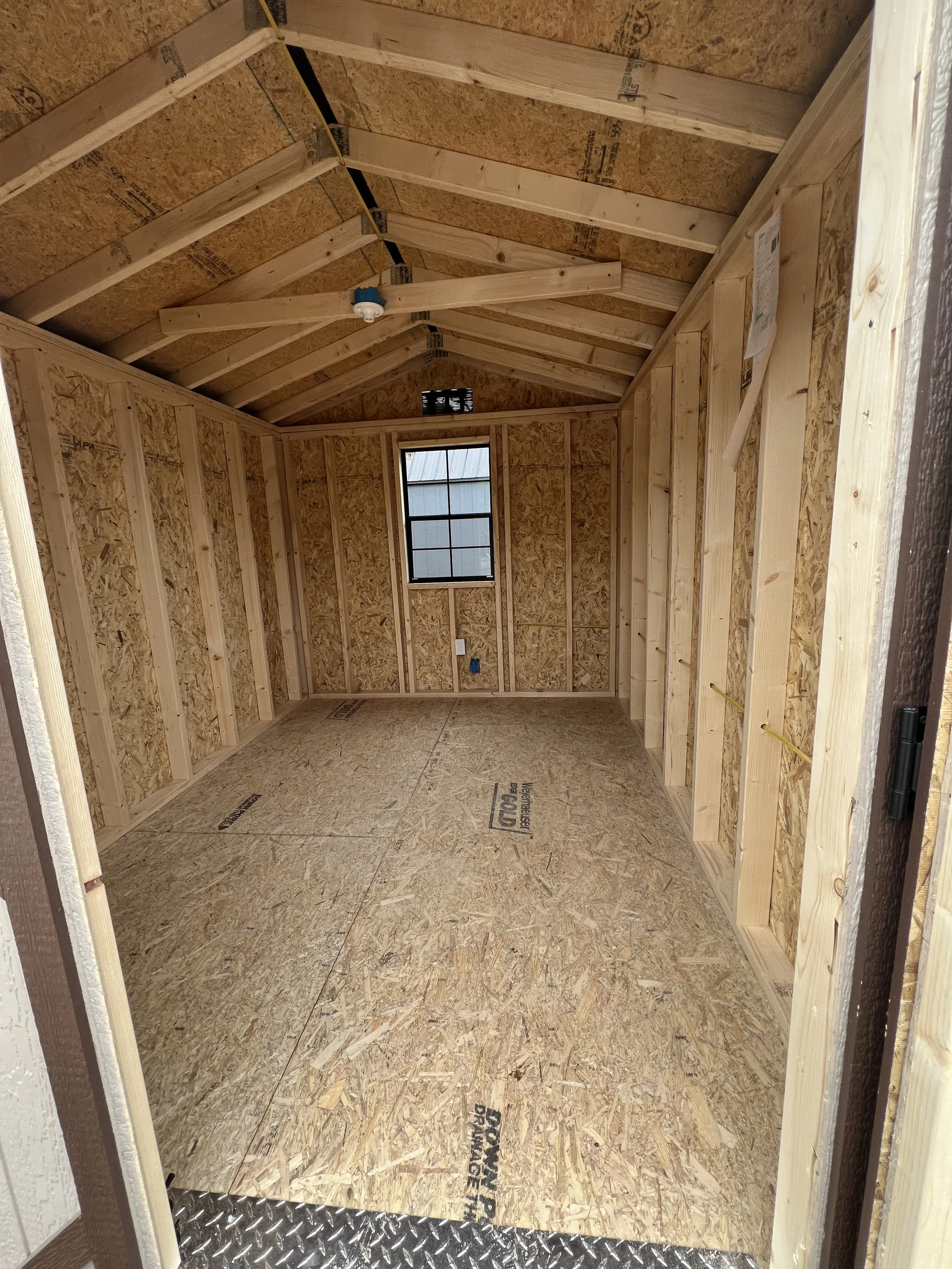 Interior of an unfinished wooden shed with exposed beams and a small window.
