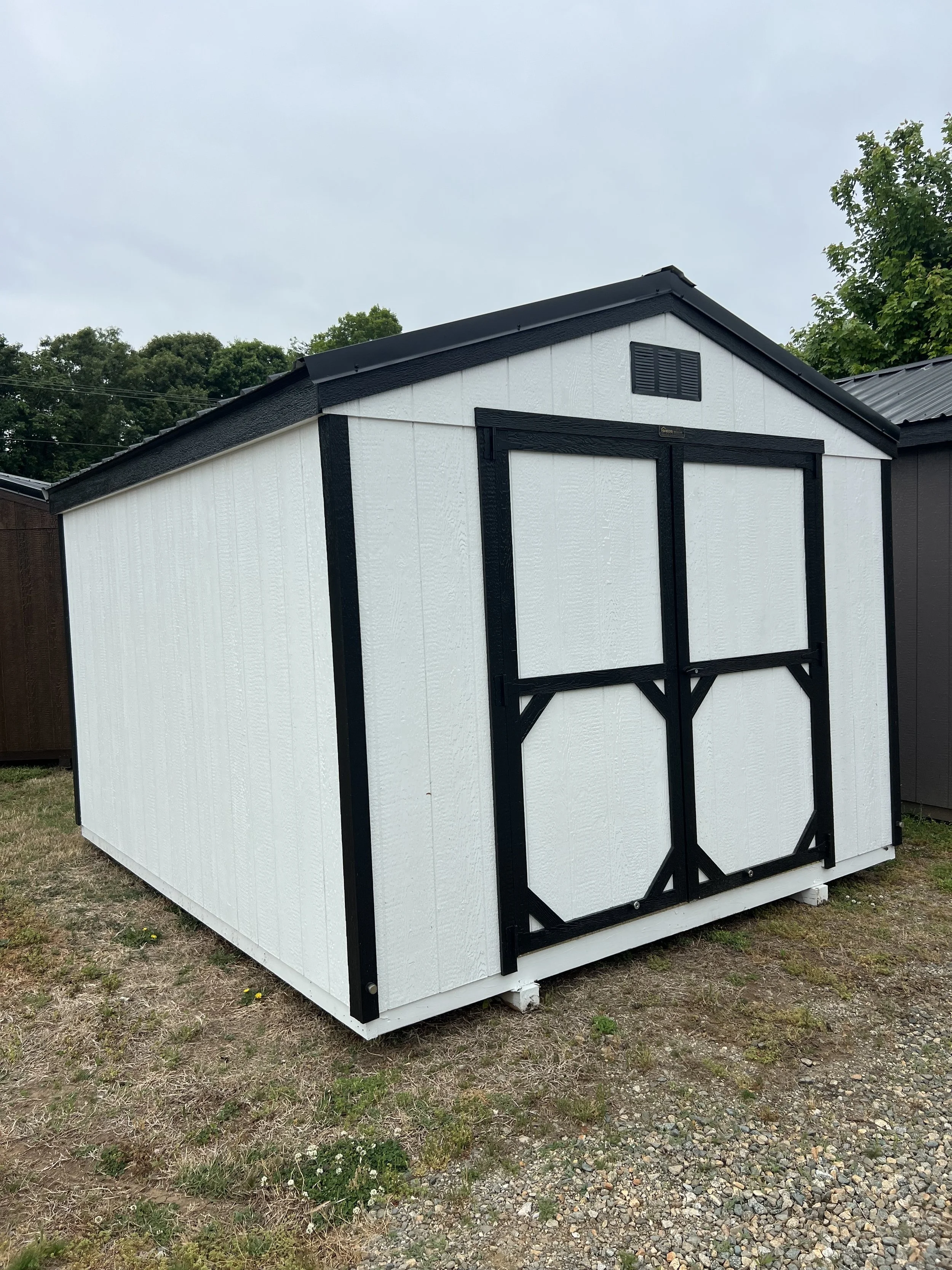 Wooden storage shed with double doors and a charcoal metal roof, located inside a warehouse.
