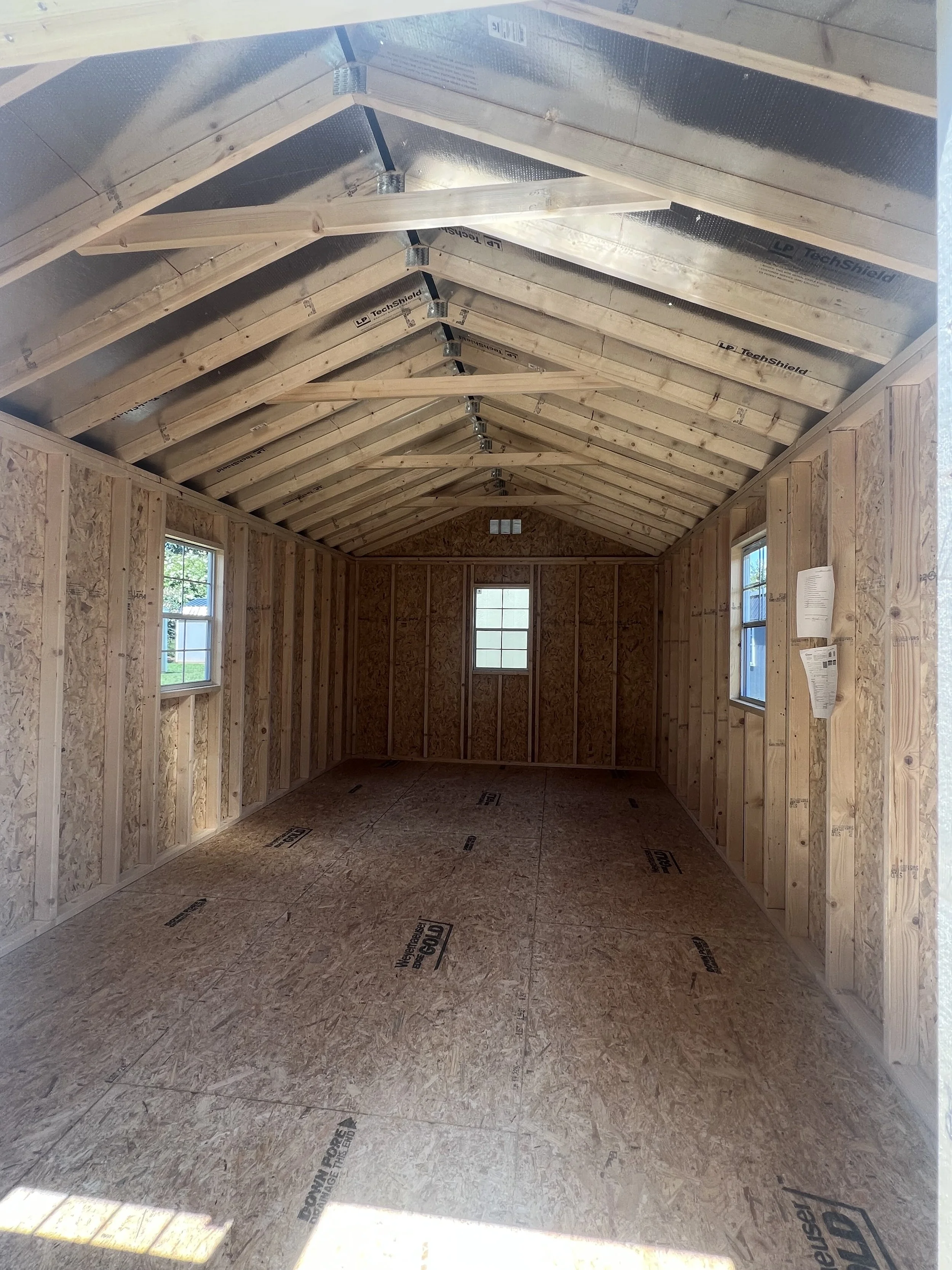 Interior of an unfinished wooden shed with exposed framing and walls, featuring a gable roof structure