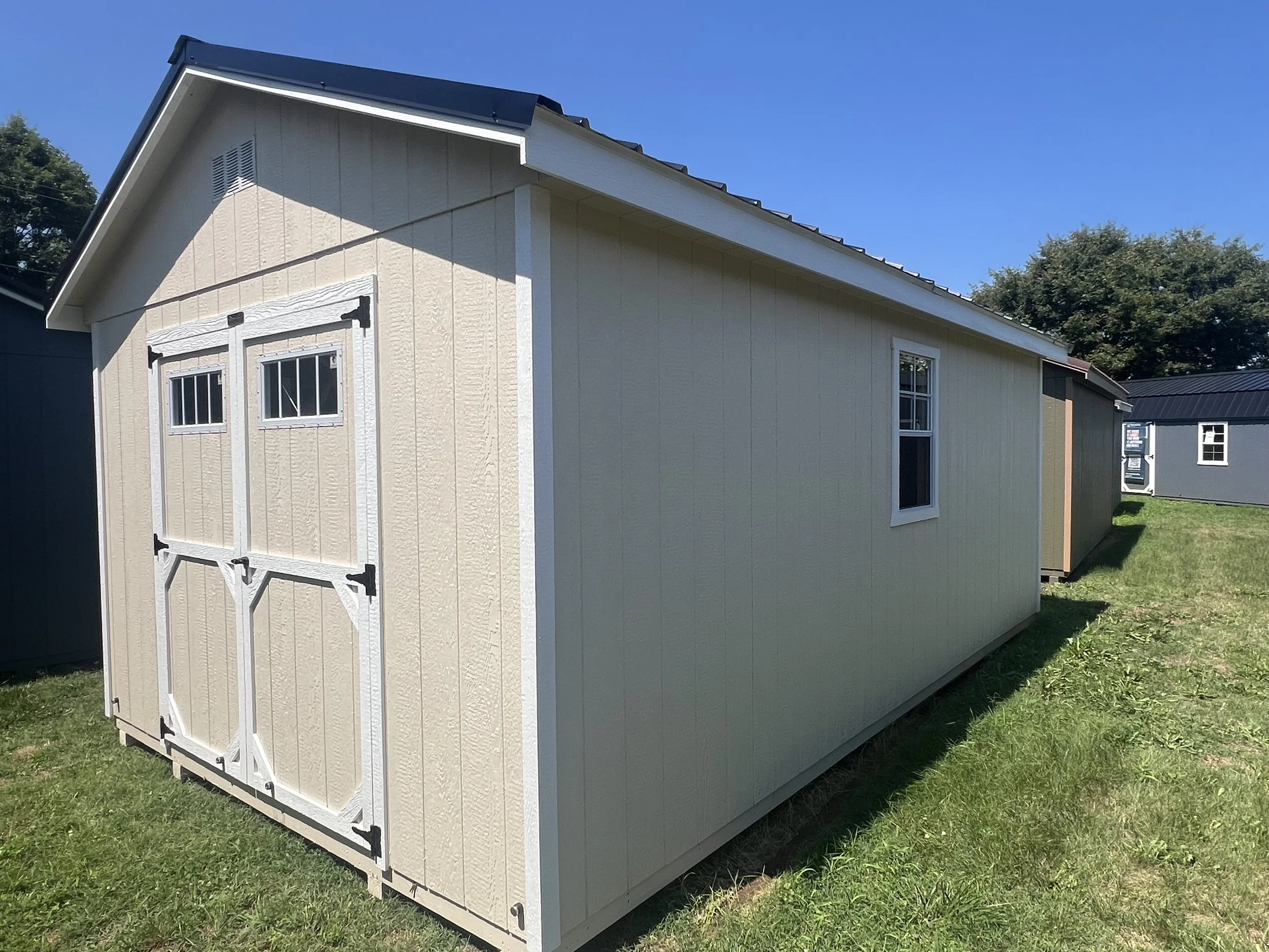 Portable building with black metal roof and almond siding