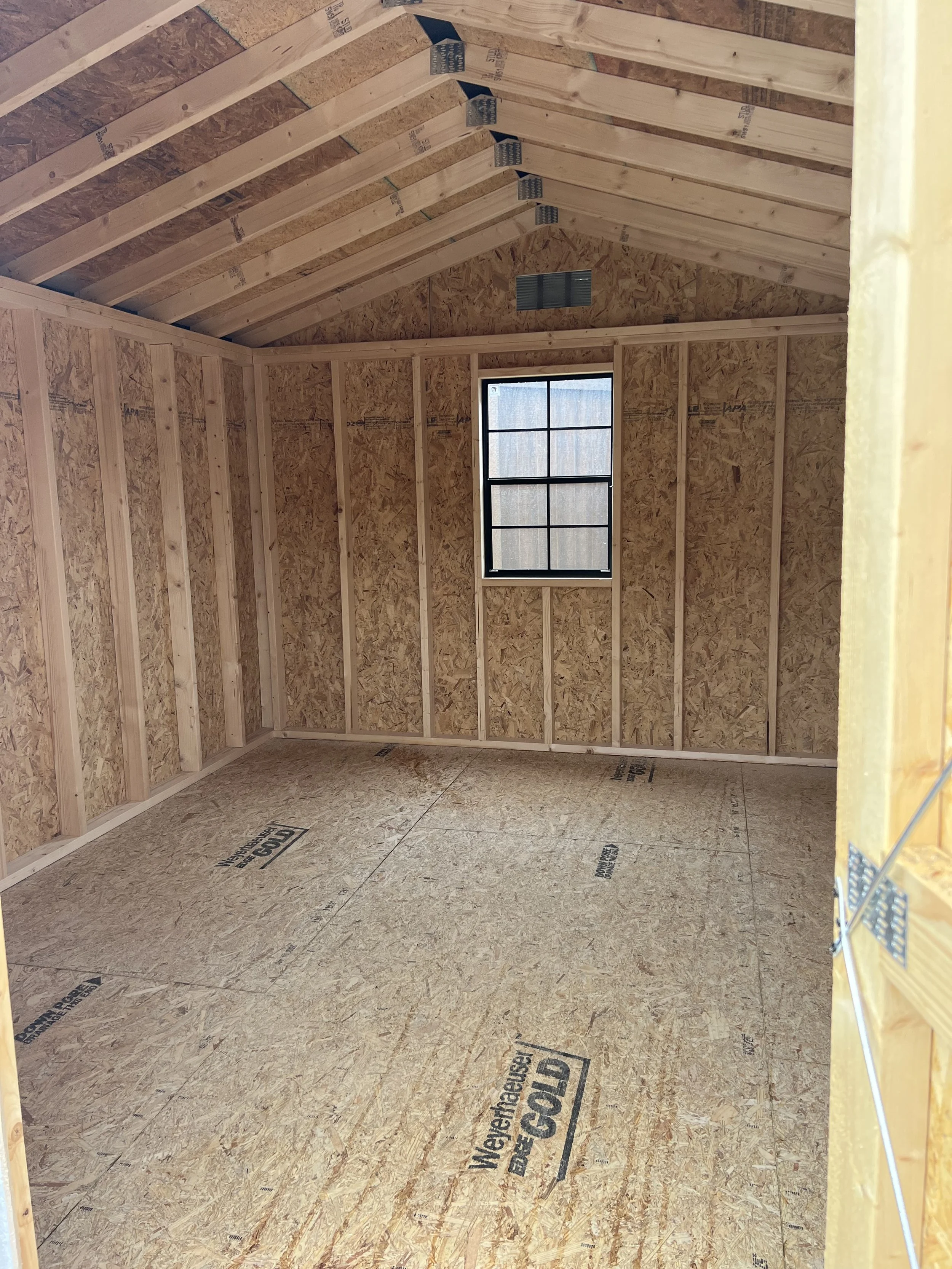 Interior of an unfinished wooden shed with visible framing and a loft area.