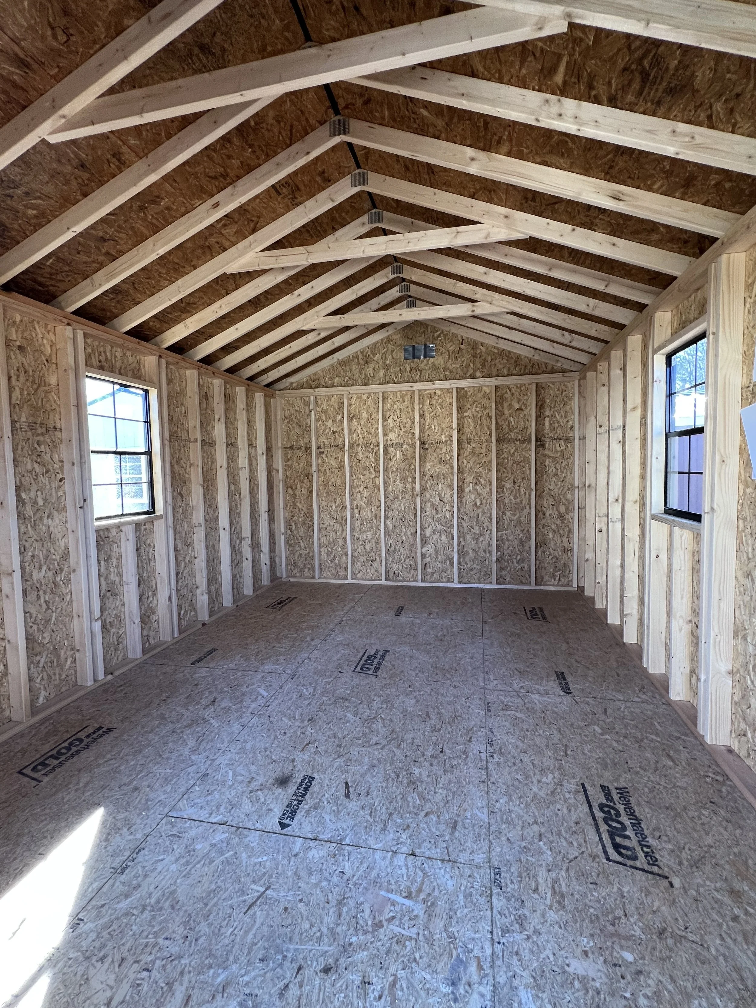 Interior of an unfinished wooden shed with visible studs and a window.