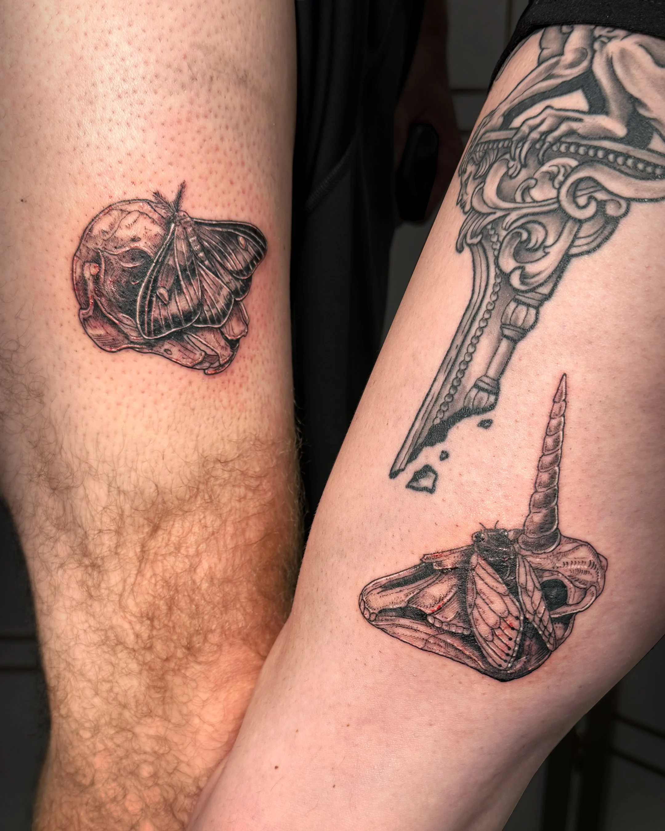 Close-up of two tattoos on arms: a butterfly on the left arm and a skeletal arm and wing on the right arm.
