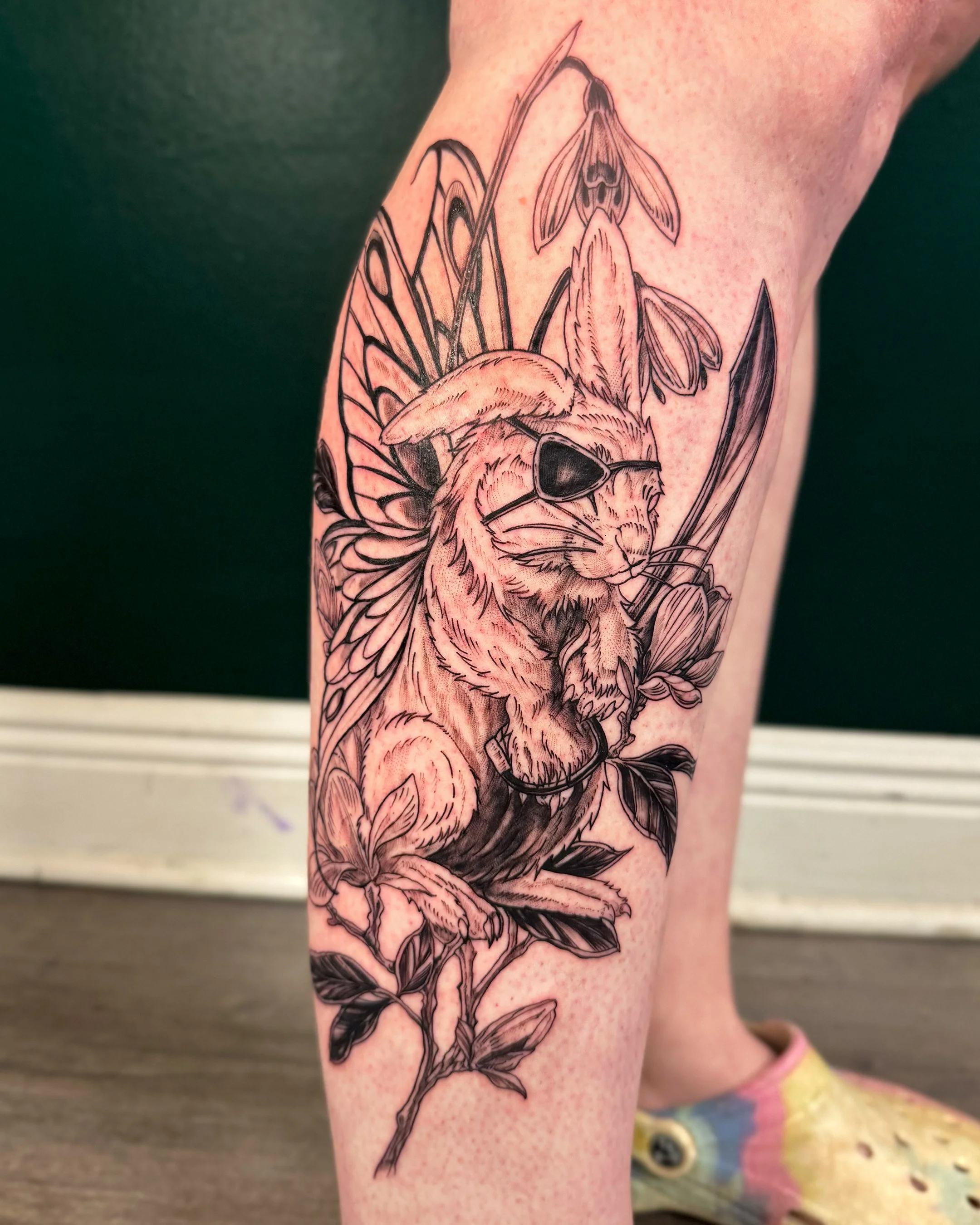 A tattoo of a bee with sunglasses and a butterfly with detailed wings, surrounded by leaves on a person's arm.