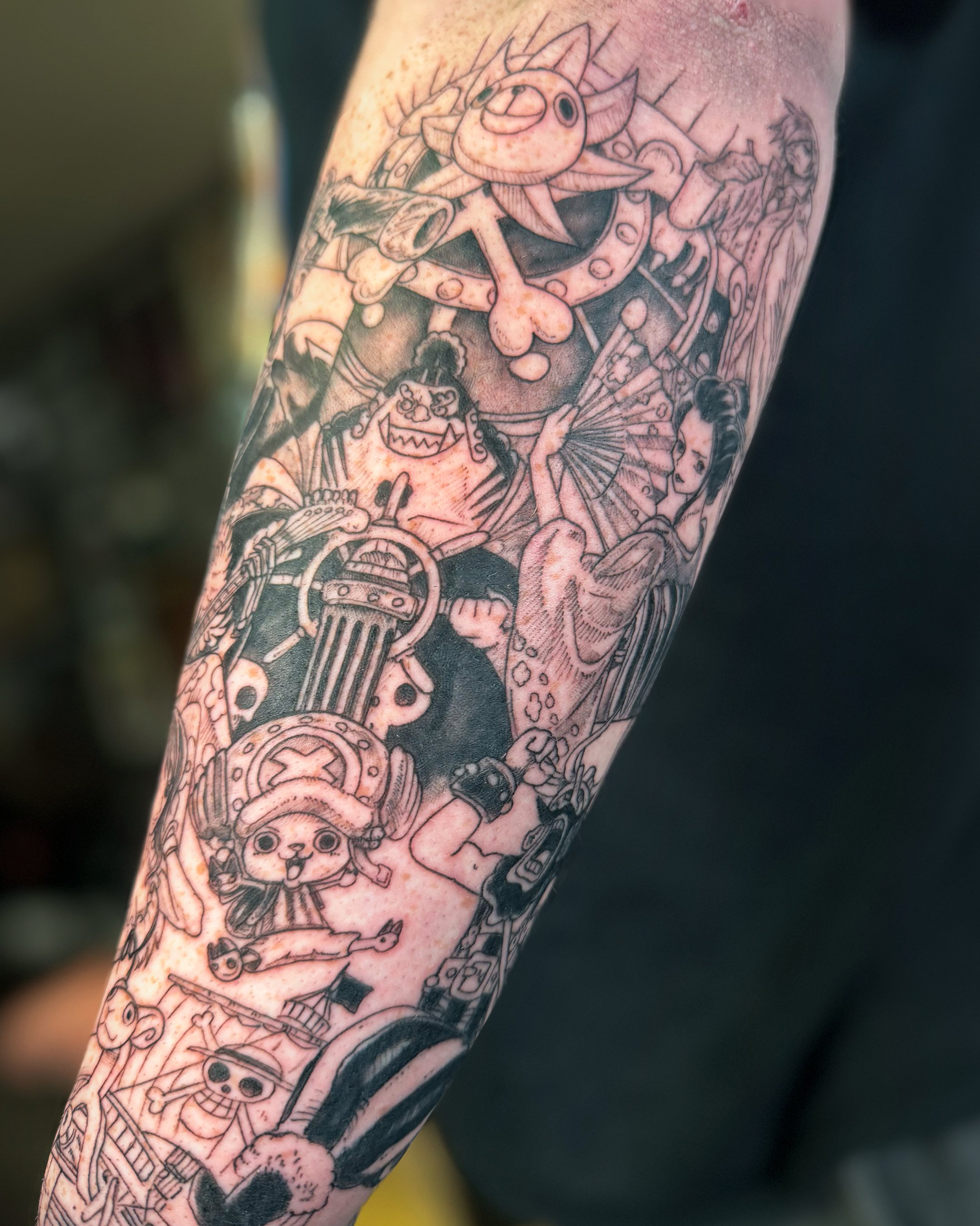 Colorful tattoo sleeve featuring a variety of cartoonish characters, including a creature with large eyes, a puppet with a mischievous grin, and a woman with a traditional hairstyle, all intertwined with mechanical and abstract elements.