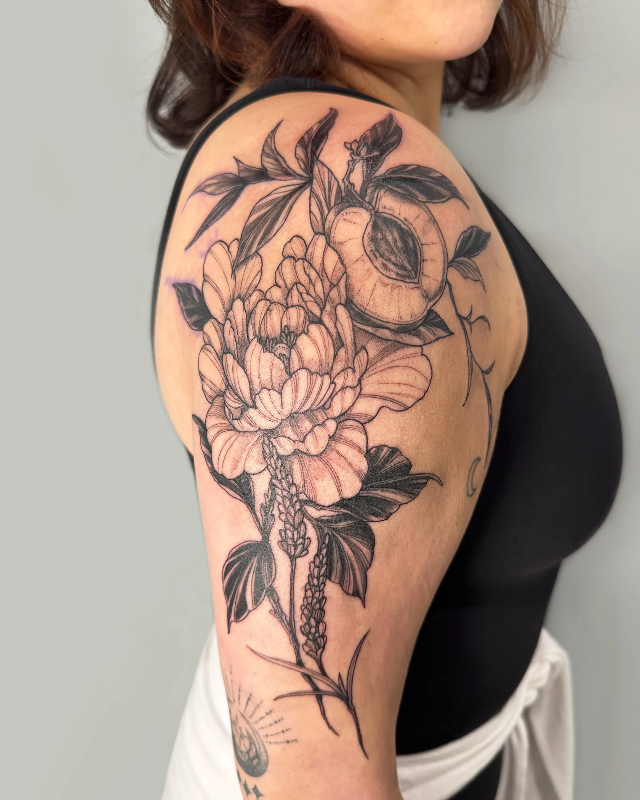 A black and gray floral tattoo on a person's upper arm and shoulder, featuring detailed blooming flowers and leaves, with some shading and line work.