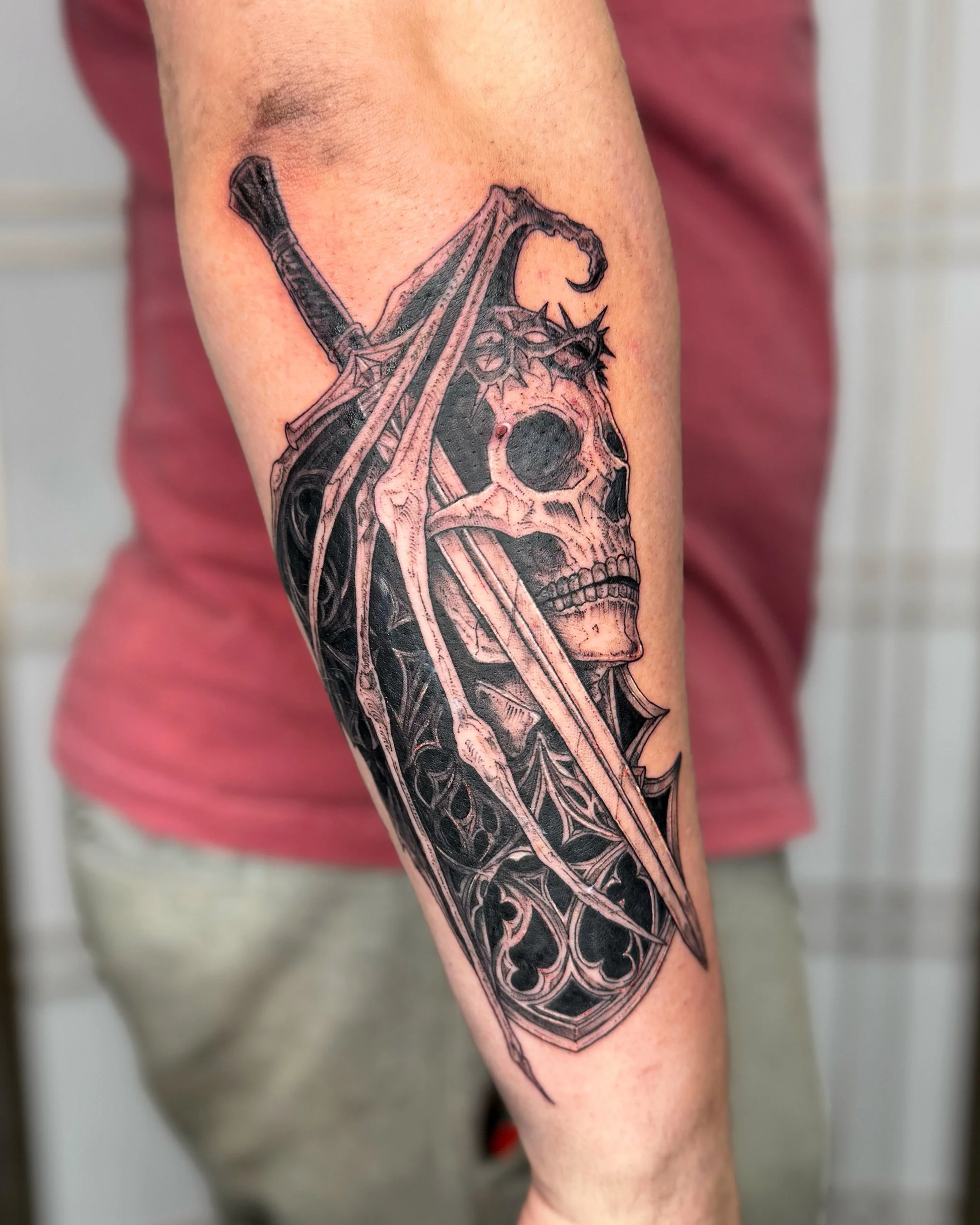 Tattoo of a detailed skull with a sword running vertically through it, on person's forearm.