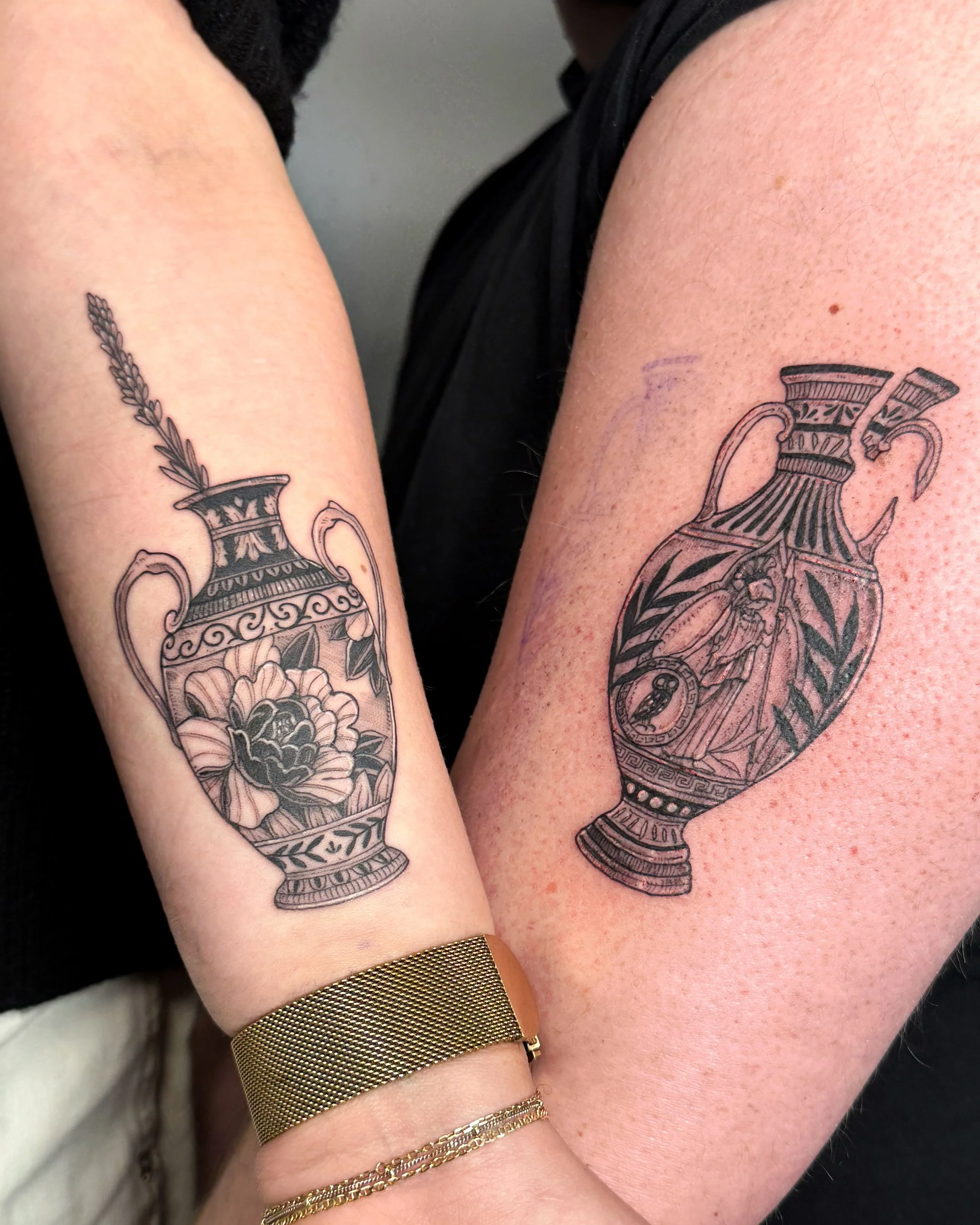 Close-up of people's arms with tattoos of ornate vases and flowers, some wearing gold jewelry.