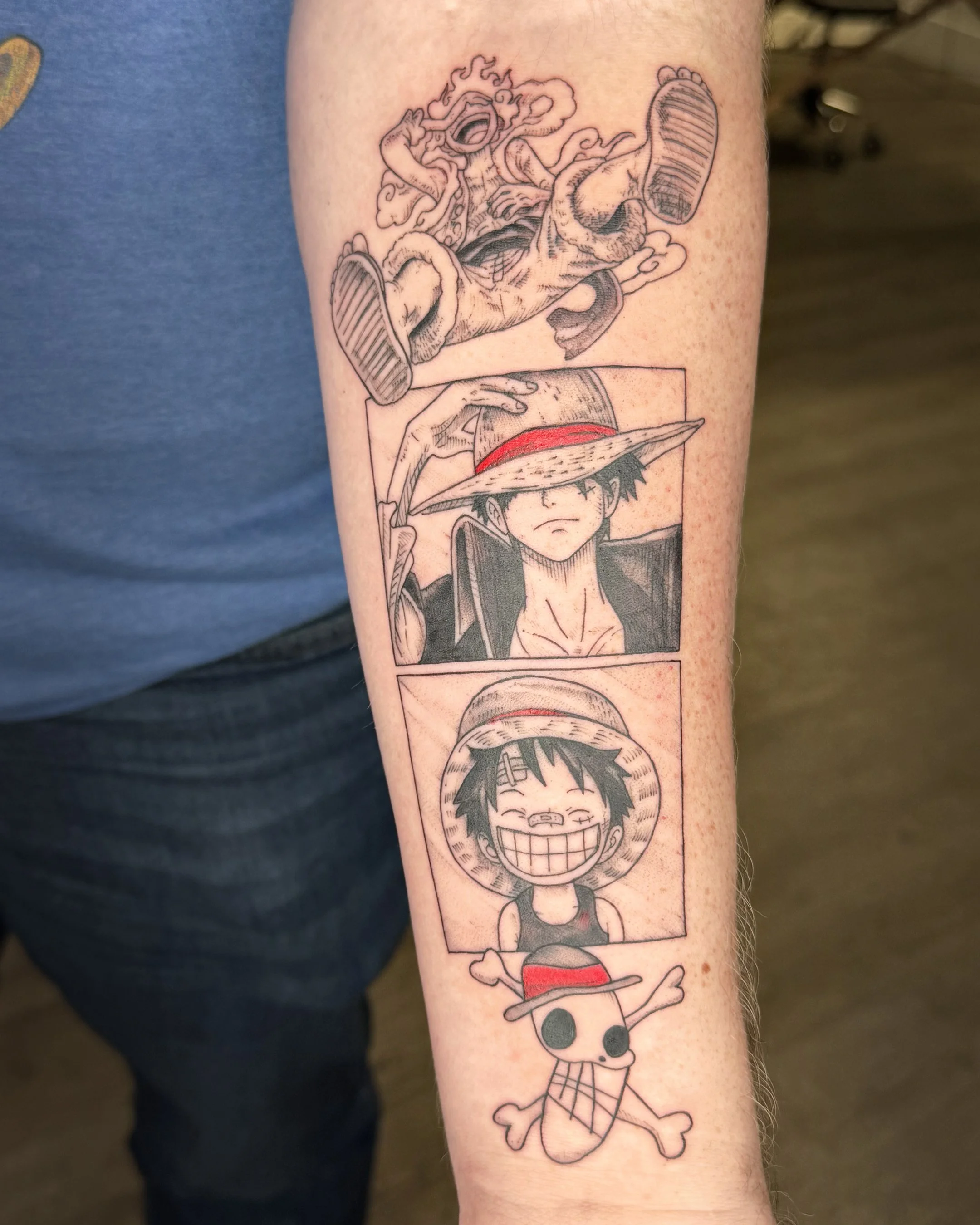Tattoo featuring a cartoon character with glasses and a big smile, on a body with a visible arm. The character is holding a straw hat with a red band, and there is a manga-style scene with a person flying through clouds above.