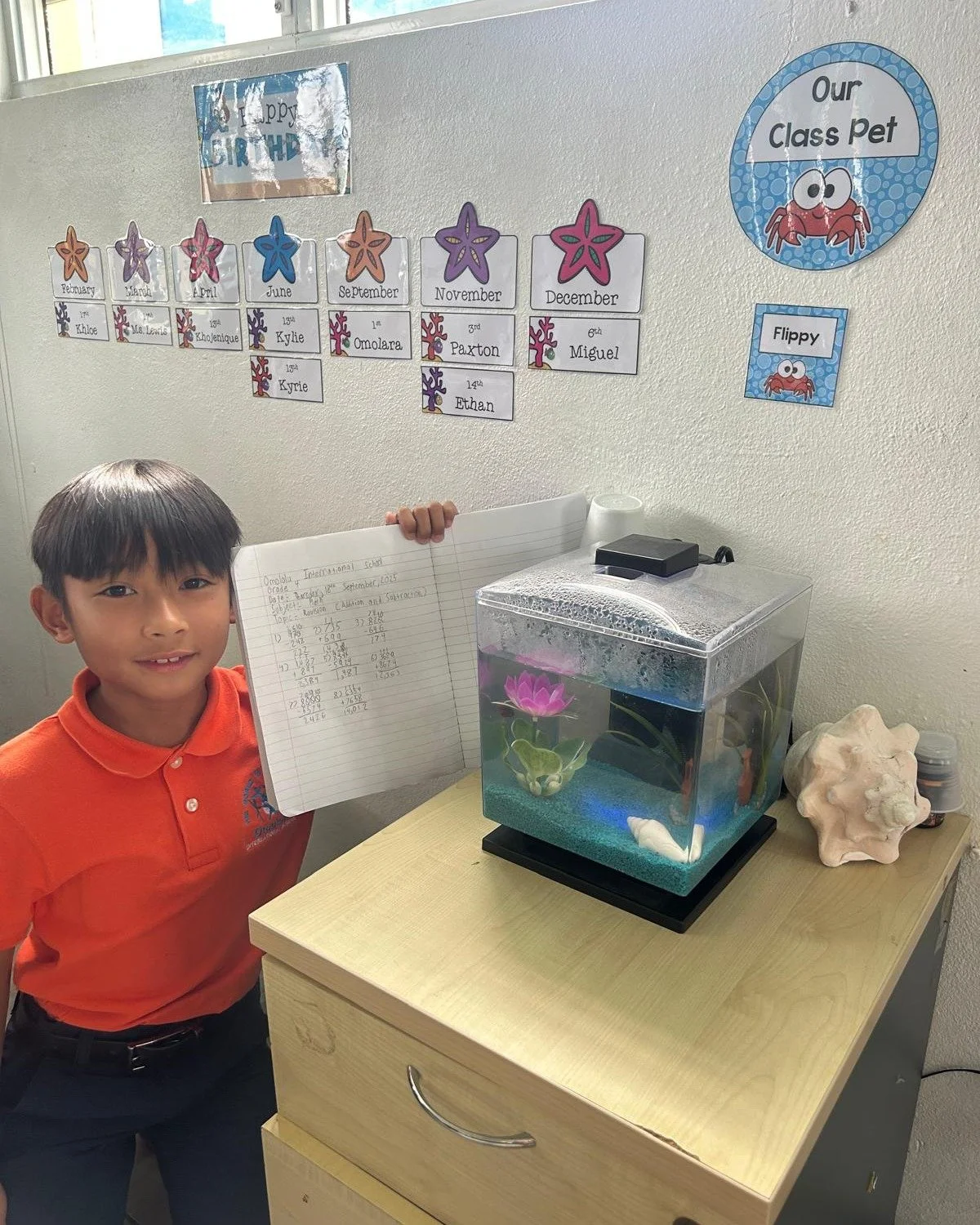 Grade 4 has a class pet! Here is one of the Omololu International School 4th Graders sharing his math work with Flippy the Fourth Grade Fish!