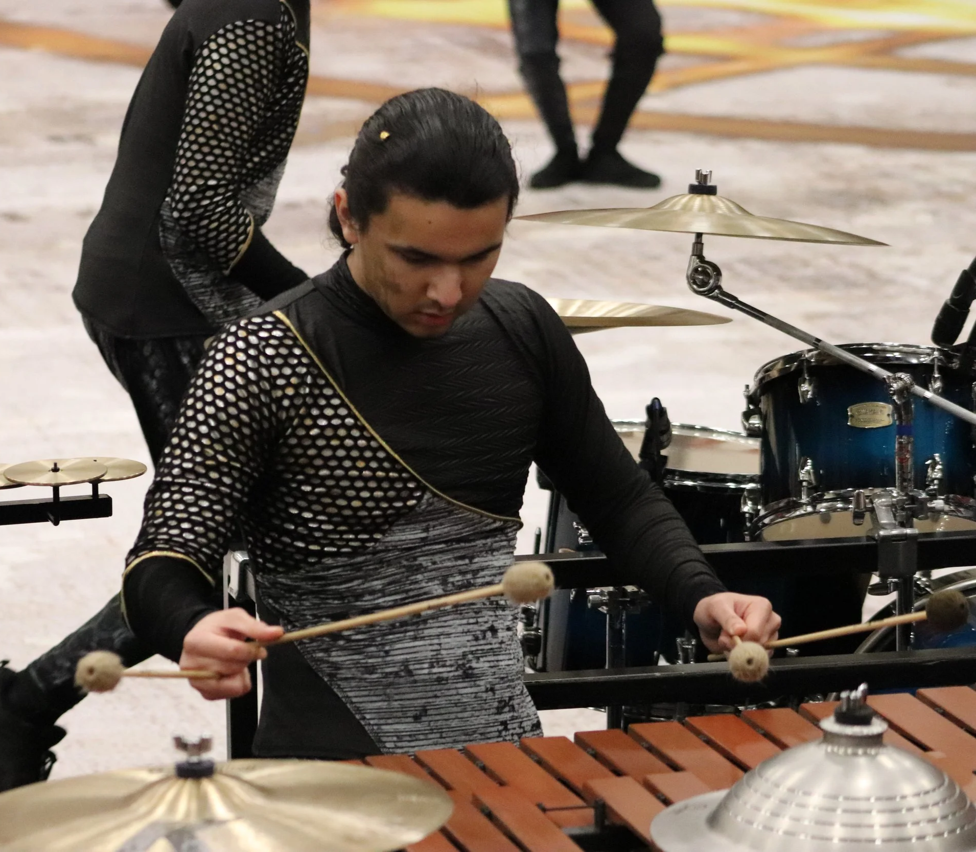 A musician playing a marimba during a winter percussion drumline performance, with drums and cymbals nearby.