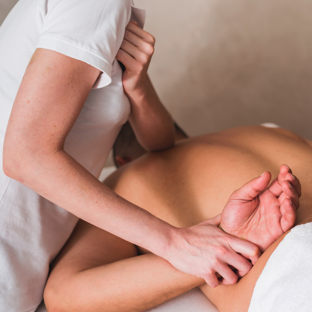A massage therapist giving a massage to a person lying face down on a massage table.