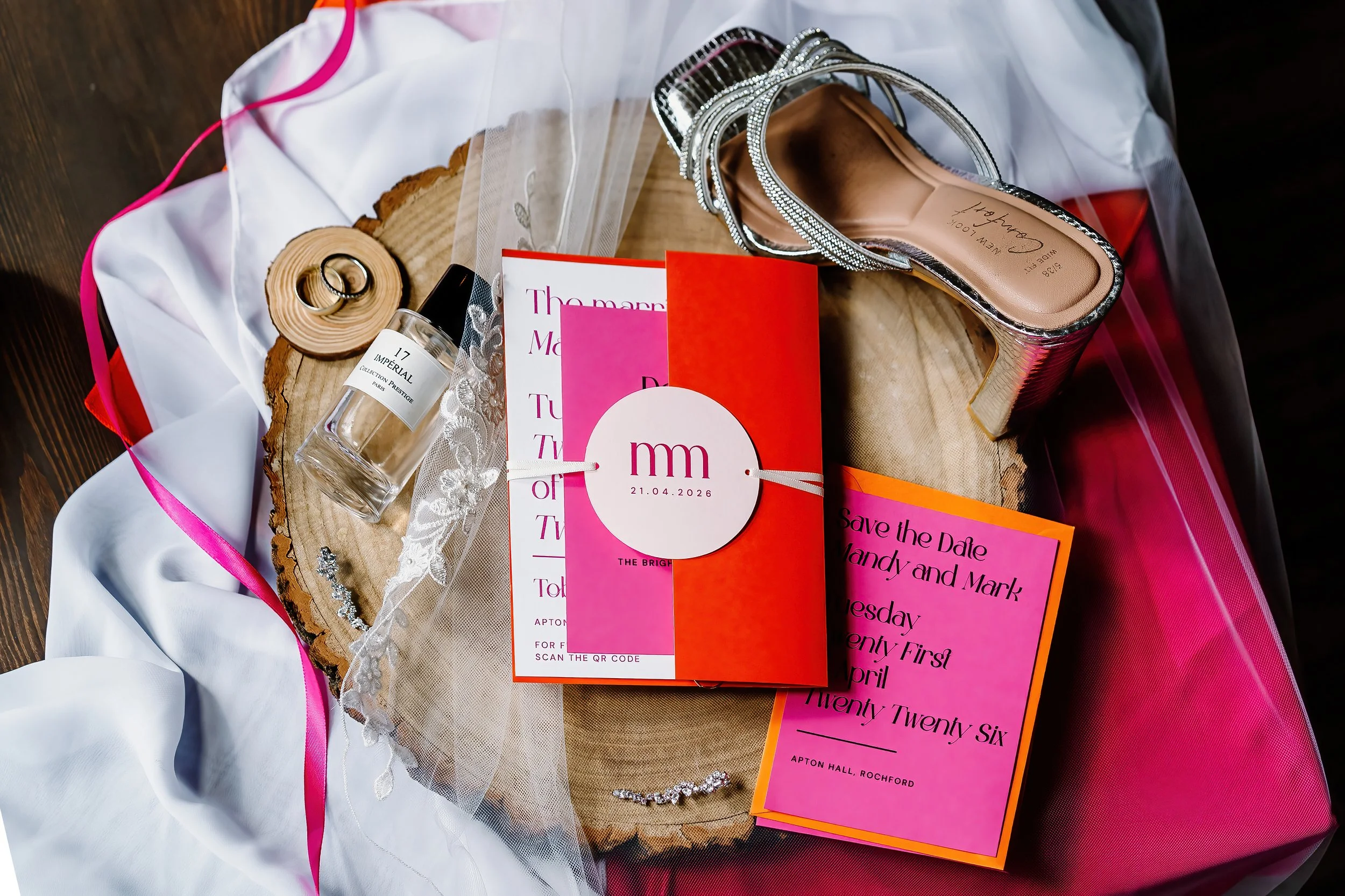 Vibrant orange and pink  wedding invitation showing Bride shoes, couples rings and perfume