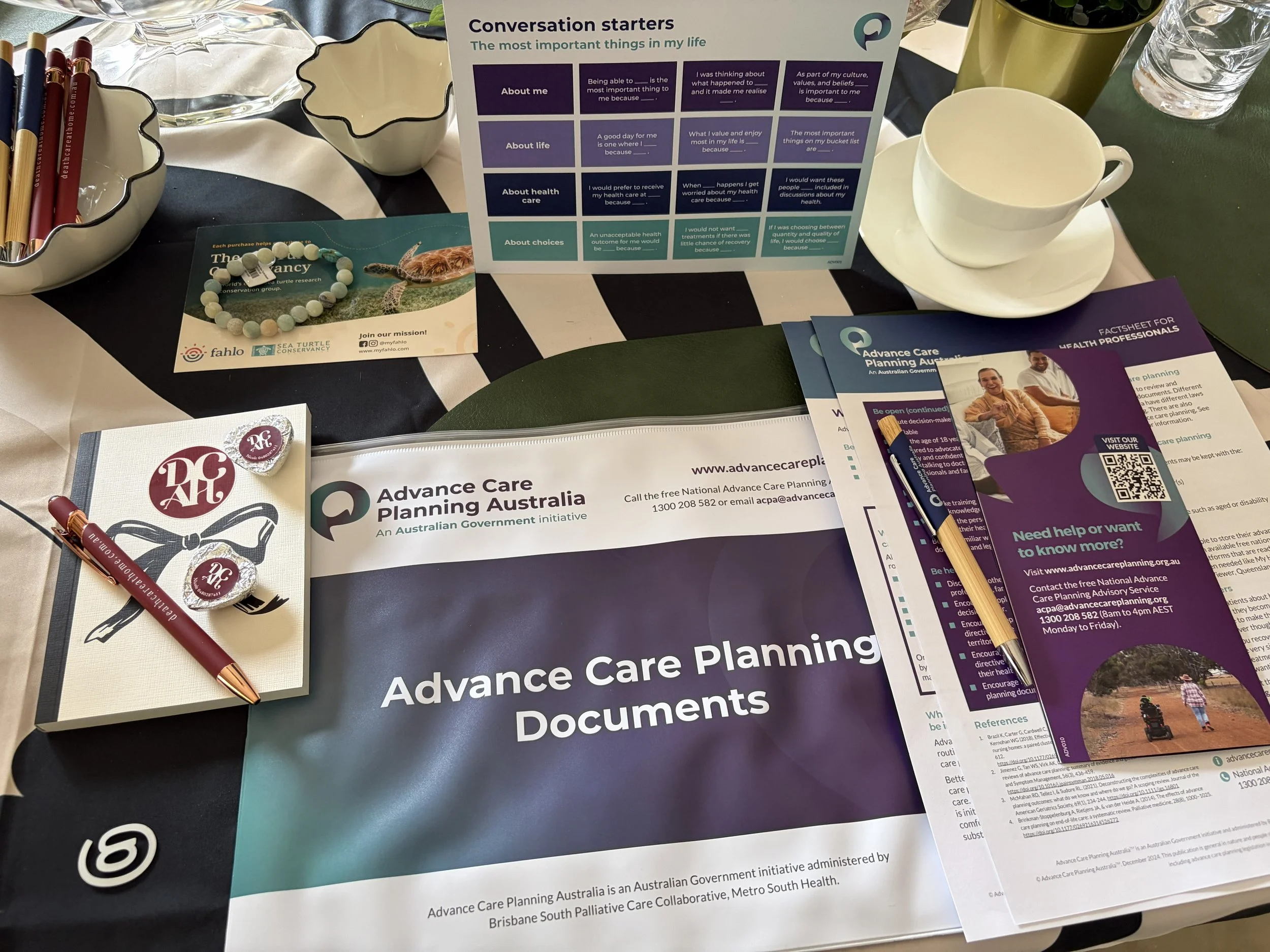 Table with brochures, flyers, and informational materials about advance care planning and healthcare services, including discussion starters, brochures from Fahlo Sea Turtle Conservancy, and promotional pens and wristbands.