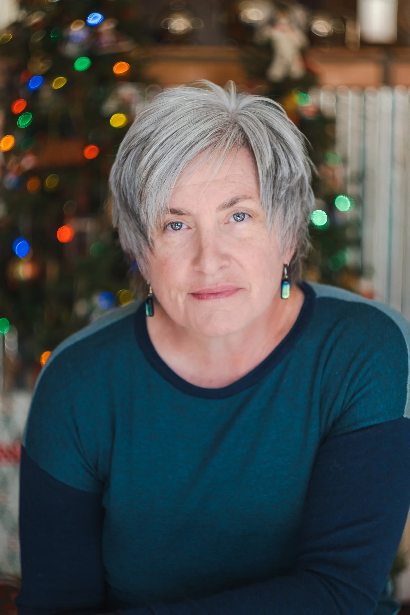 Person with gray hair in blue shirt in front of Christmas lights.