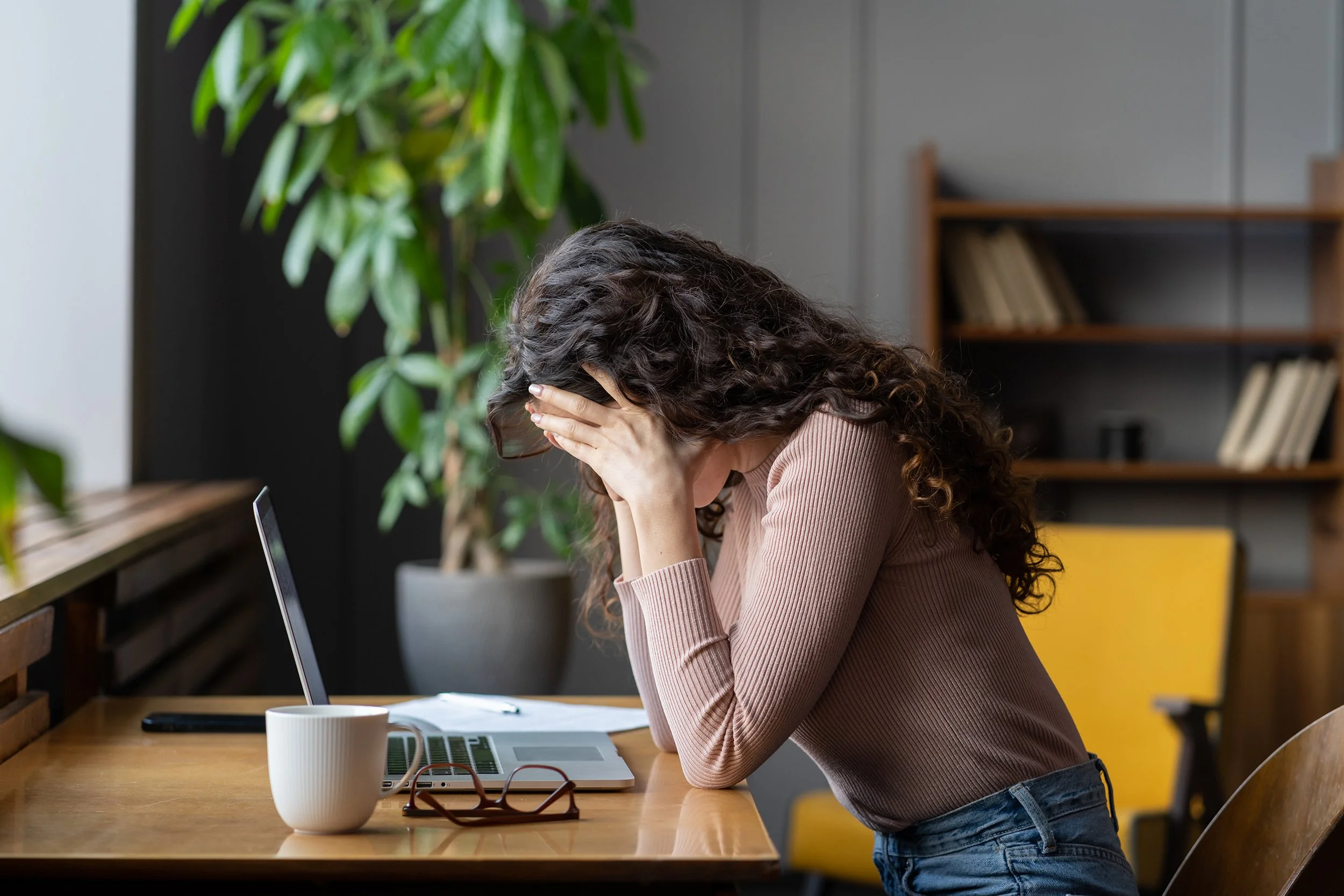A woman hunches over her computer. If Meta layoffs hit, your next moves matter. Learn how to protect your 401(k), RSUs, and retirement timeline before signing anything.