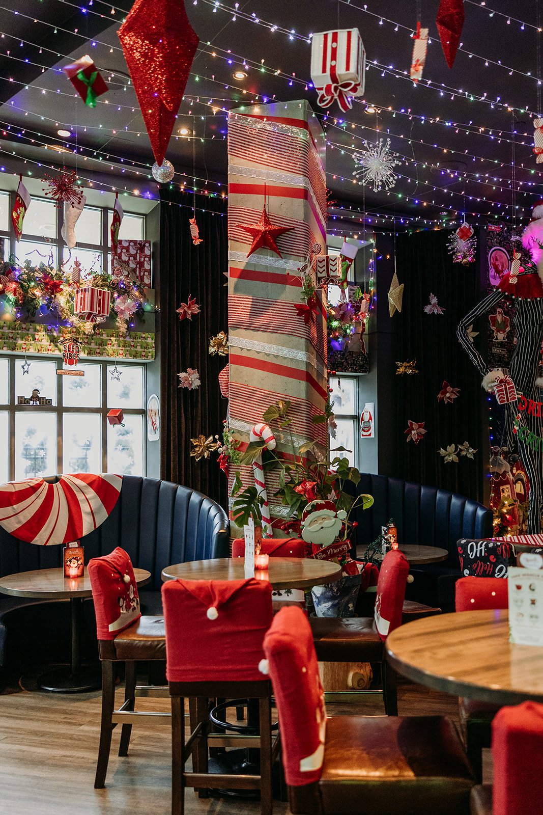 The Raven Room restaurant decorated for Christmas with hanging lights, ornaments, wrapped gifts, Santa decorations, and red velvet chairs with Christmas themed covers for Miracle Pop Up Bar in Whistler BC Canada