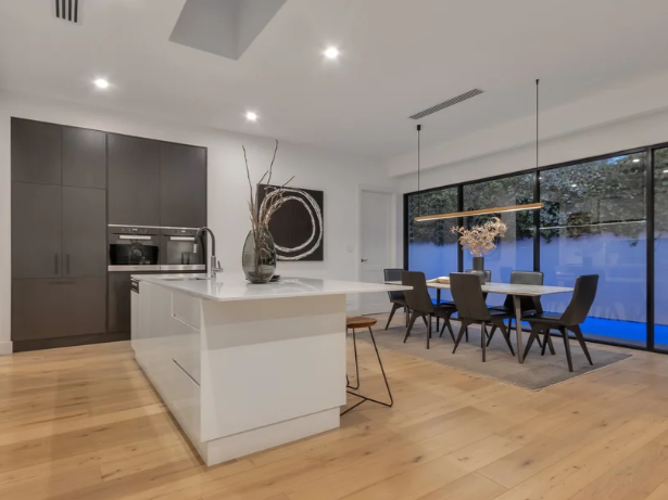 Modern Beaumont open-concept kitchen and dining area remodel in Adelaide with gray cabinets, white island, black dining chairs, large window, and minimalist decor.
