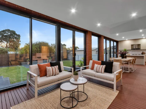 Living room with large floor-to-ceiling windows, two white sofas with black and rust-colored pillows, a round white coffee table, and a wood floor. Outside, there is a lawn and trees. Painted by Best Adelaide Painters