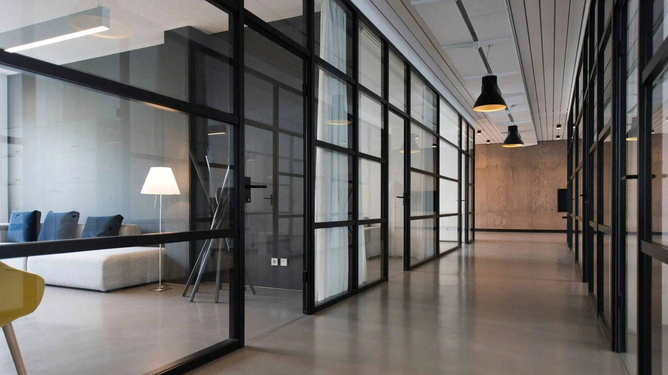 Modern office space with glass partitions, a seating area with a lamp, and wood accents for commercial painting services near Adelaide University Magill Campus Adelaide
