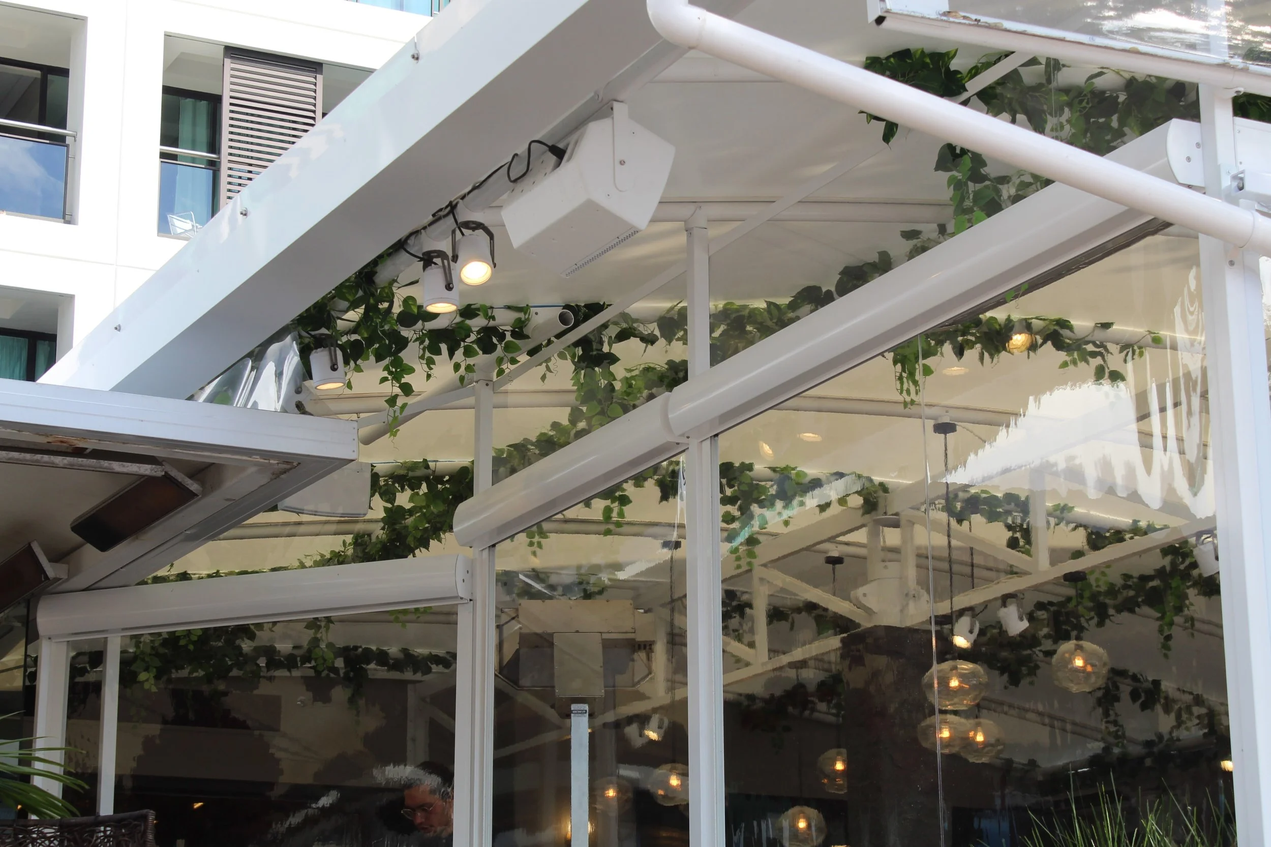 outdoor restaurant patio with glass walls, greenery, and string lights