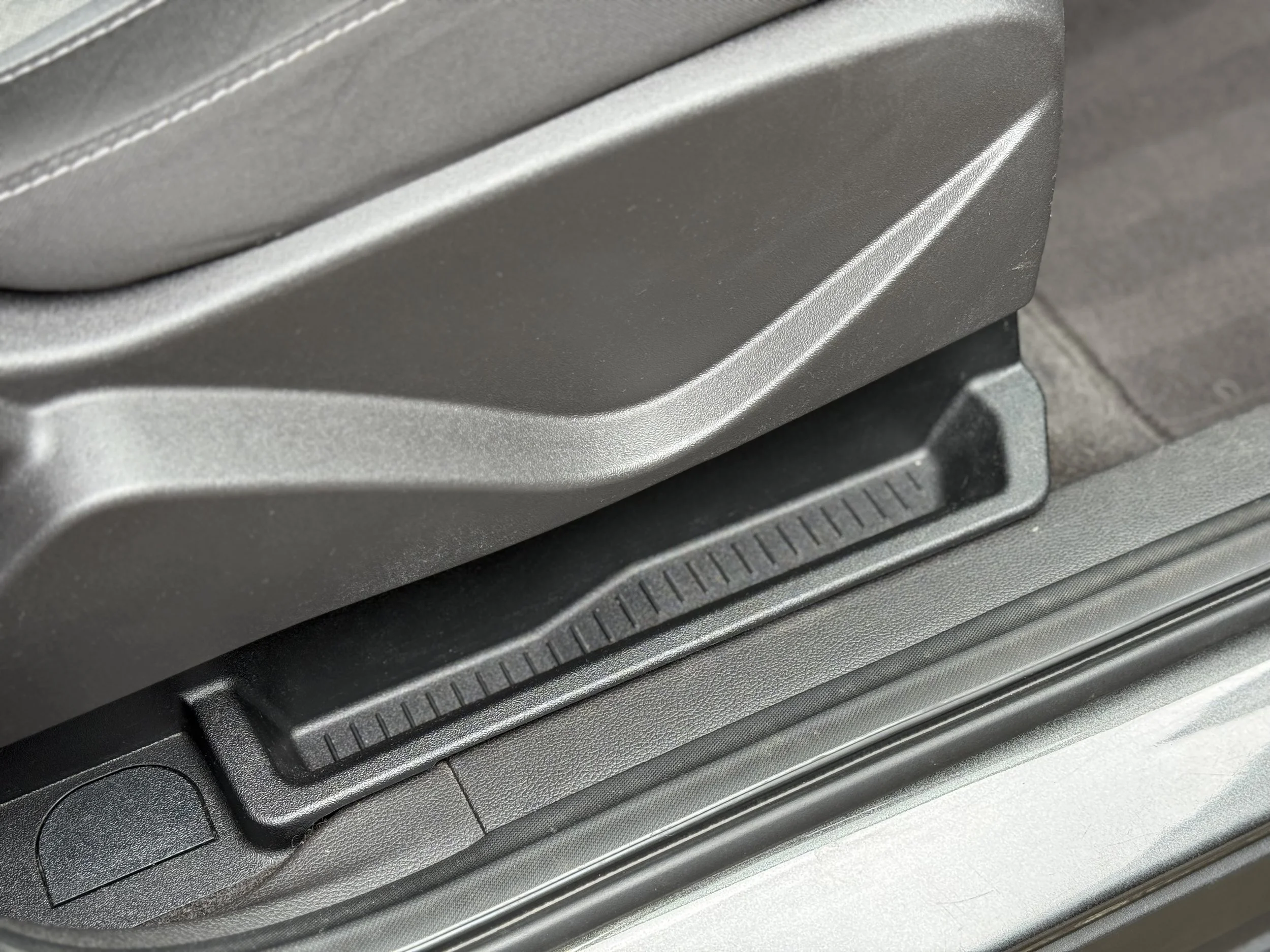 Close-up of a car seat adjustment mechanism with a textured slider and surrounding trim.