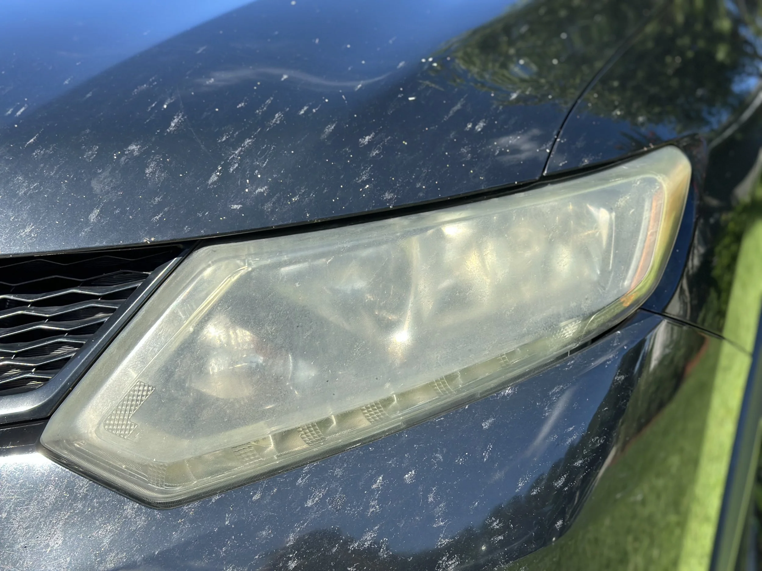 Close-up of a car's headlight and front bumper with dirt and dust on the surface.