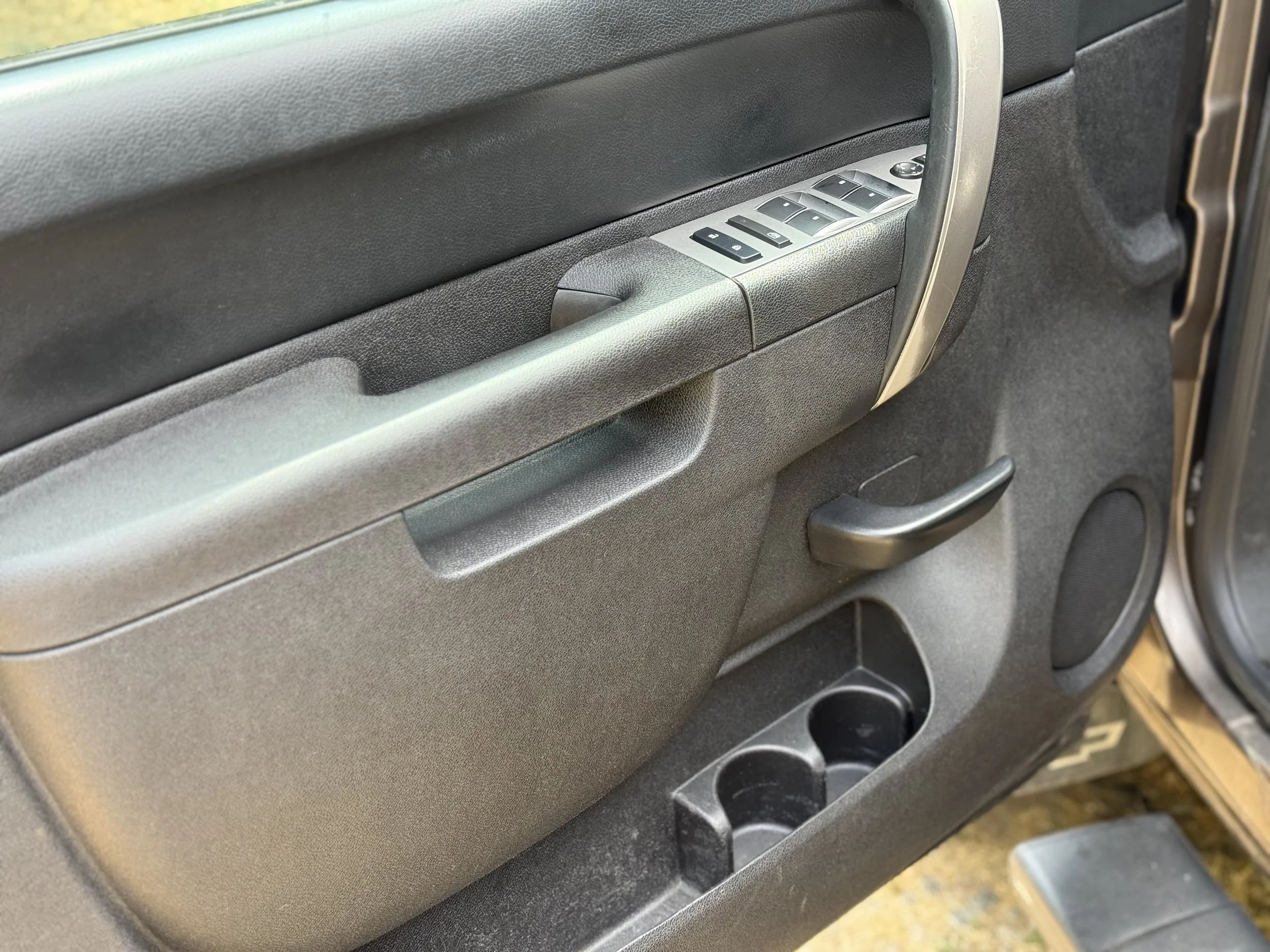 Close-up of a car door interior showing window control buttons, door handle, and a cup holder.