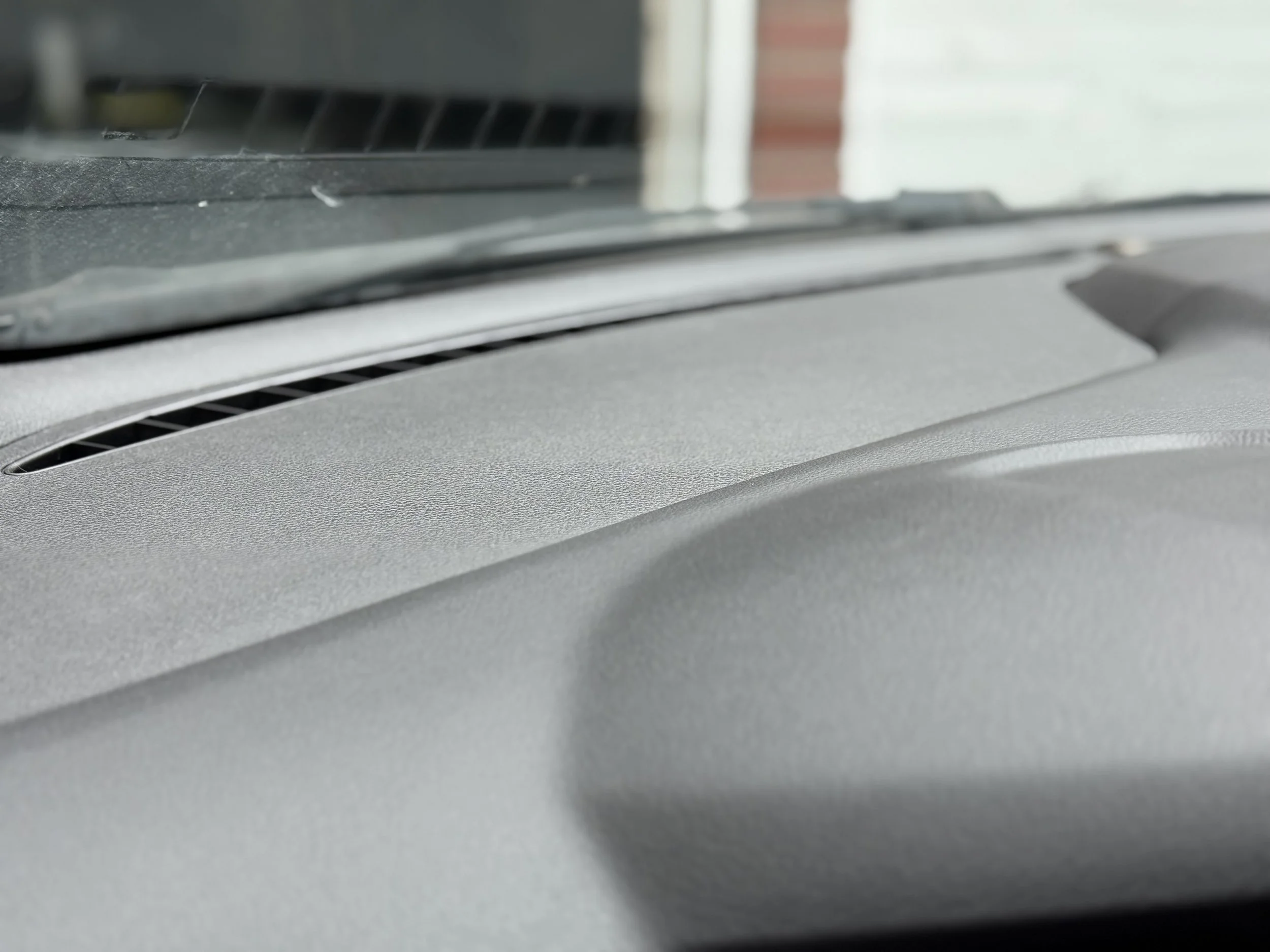 Close-up of a car dashboard showing the windshield wiper vent and part of the windshield, with some building visible outside.