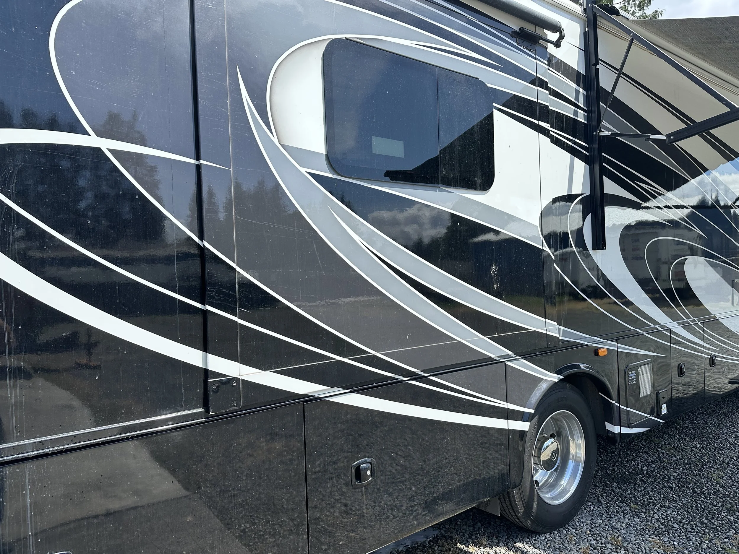 Large black motorhome with white and gray swirl designs, parked on a gravel surface.