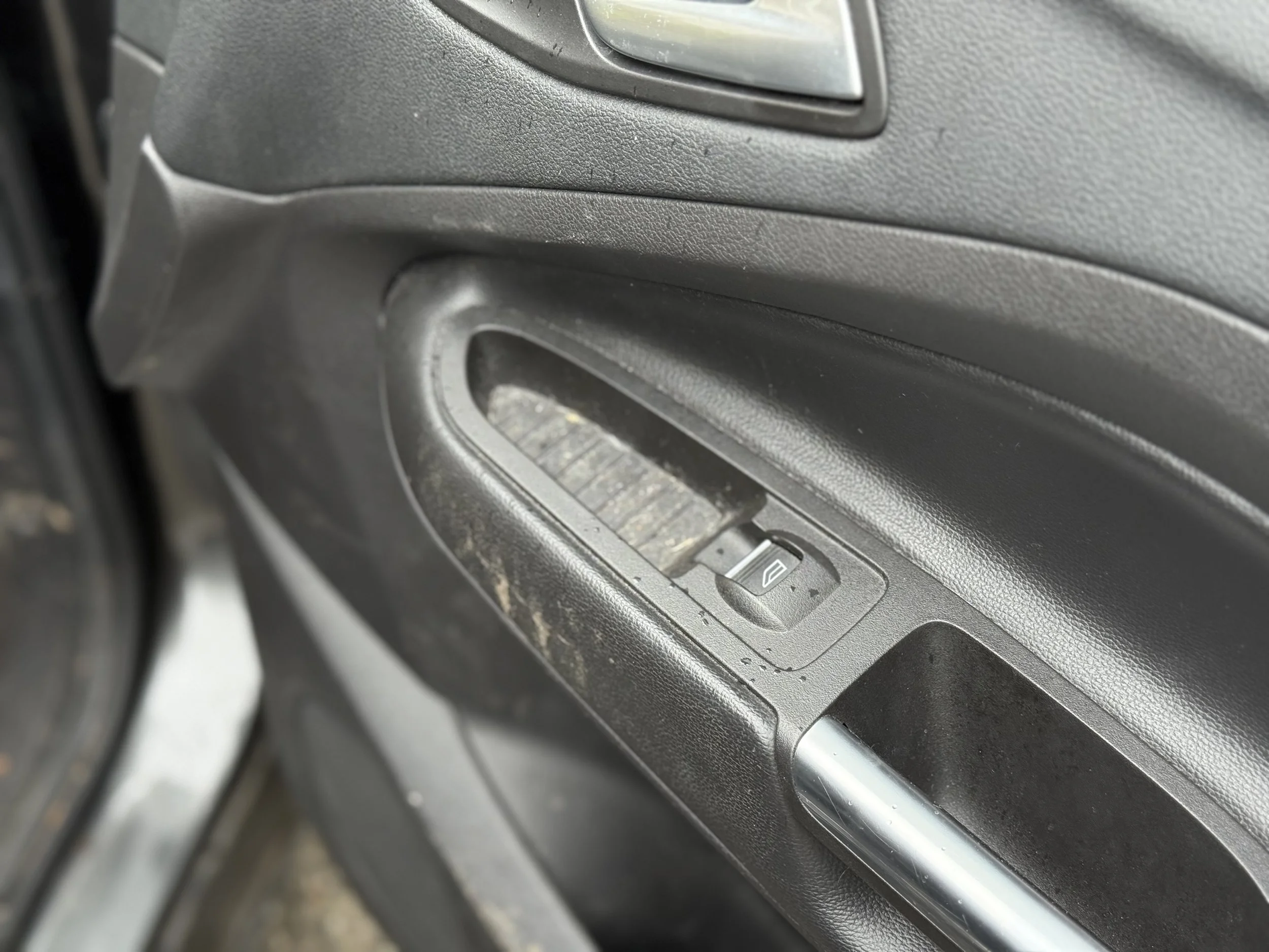 Close-up of a car door's interior with a window control switch and handle, showing signs of dirt and wear.