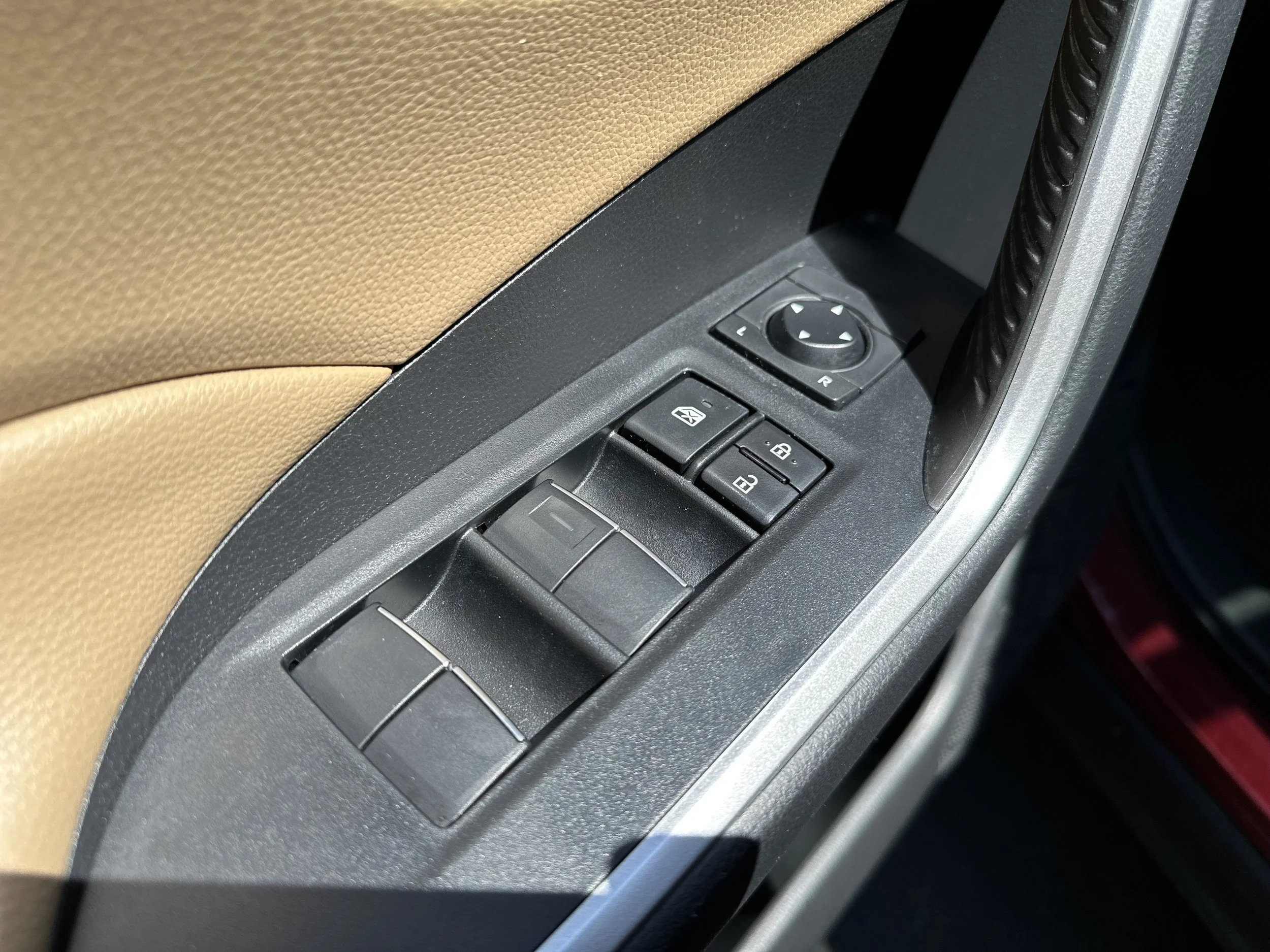 Car door control panel with window switches, lock buttons, and mirror adjustment knob.