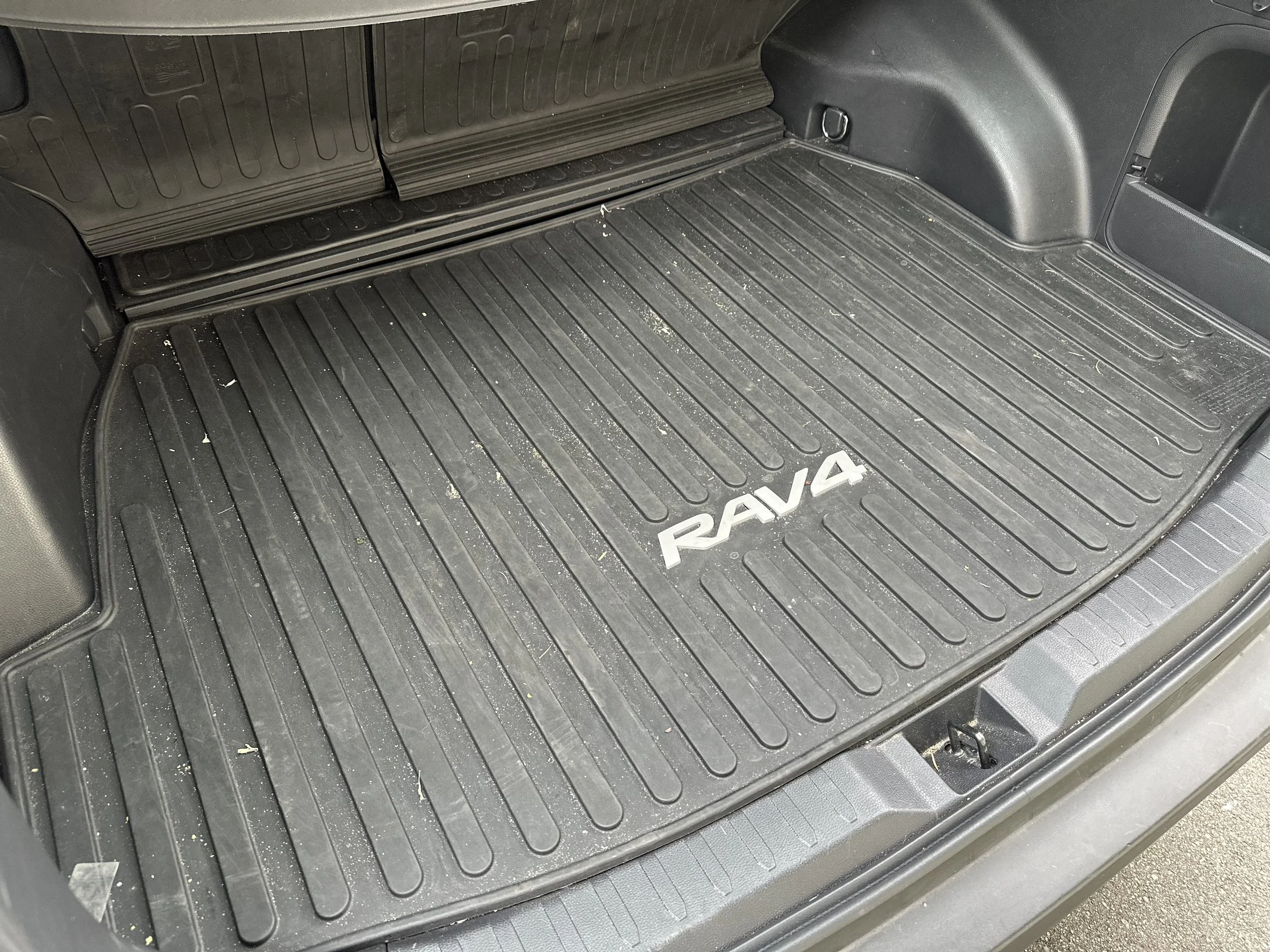 Car trunk with a rubber mat labeled RAV4, showing some dirt and debris.