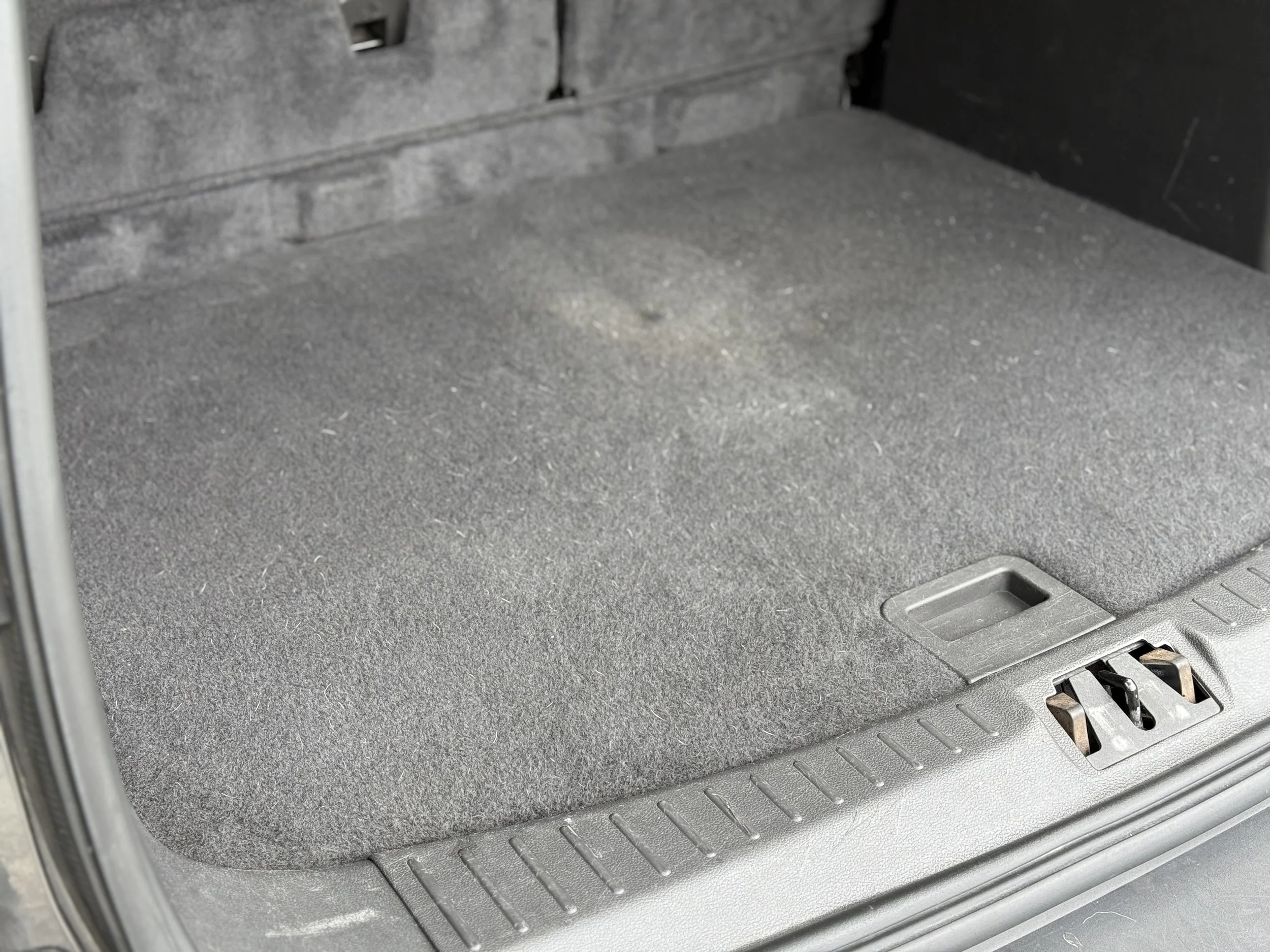 Empty car trunk with gray carpeting and a small latch.