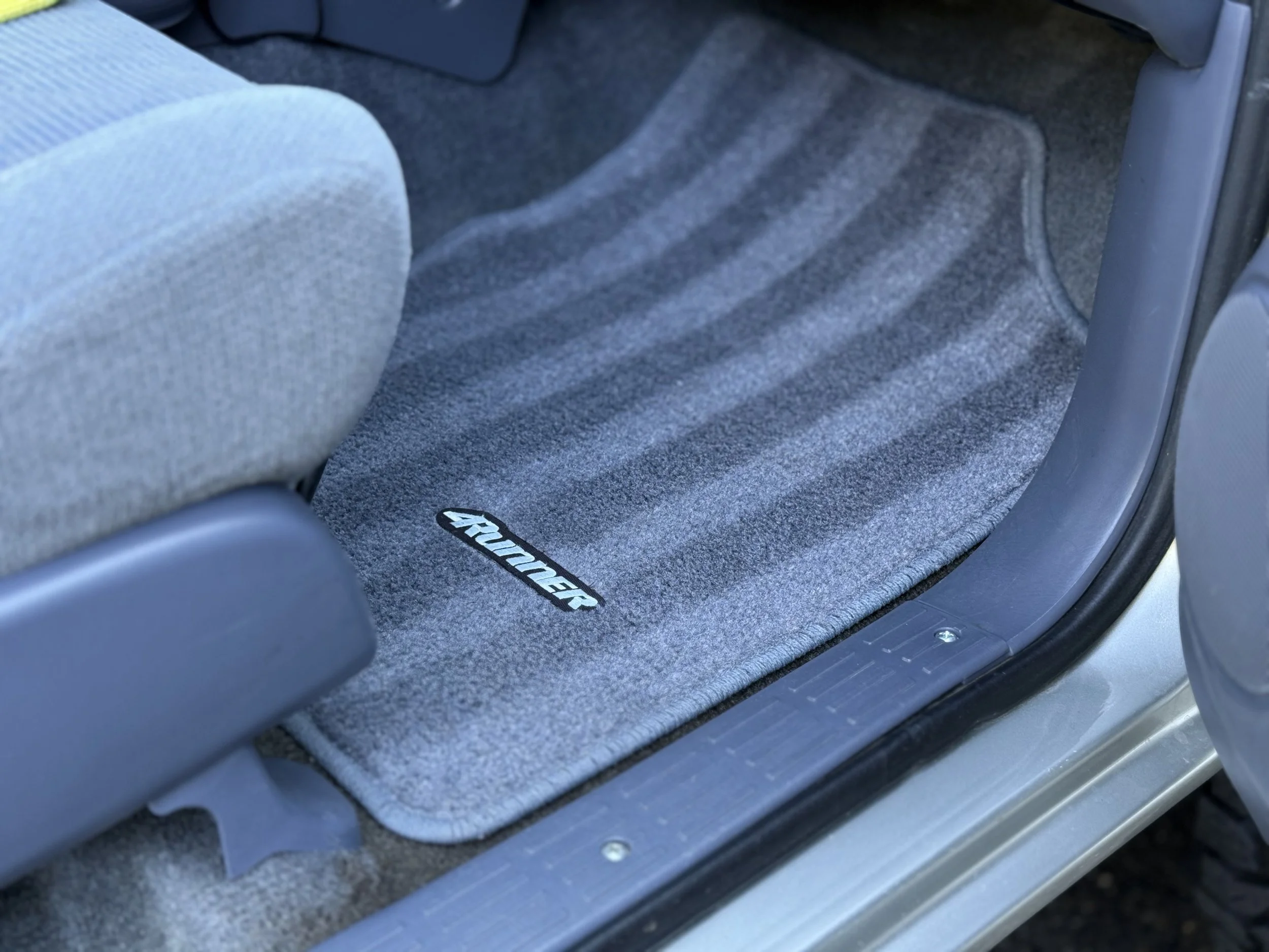 Close-up of a vehicle's gray carpeted floor mat with the word 'RANGER' embroidered on it, located in the footwell area near the passenger seat.