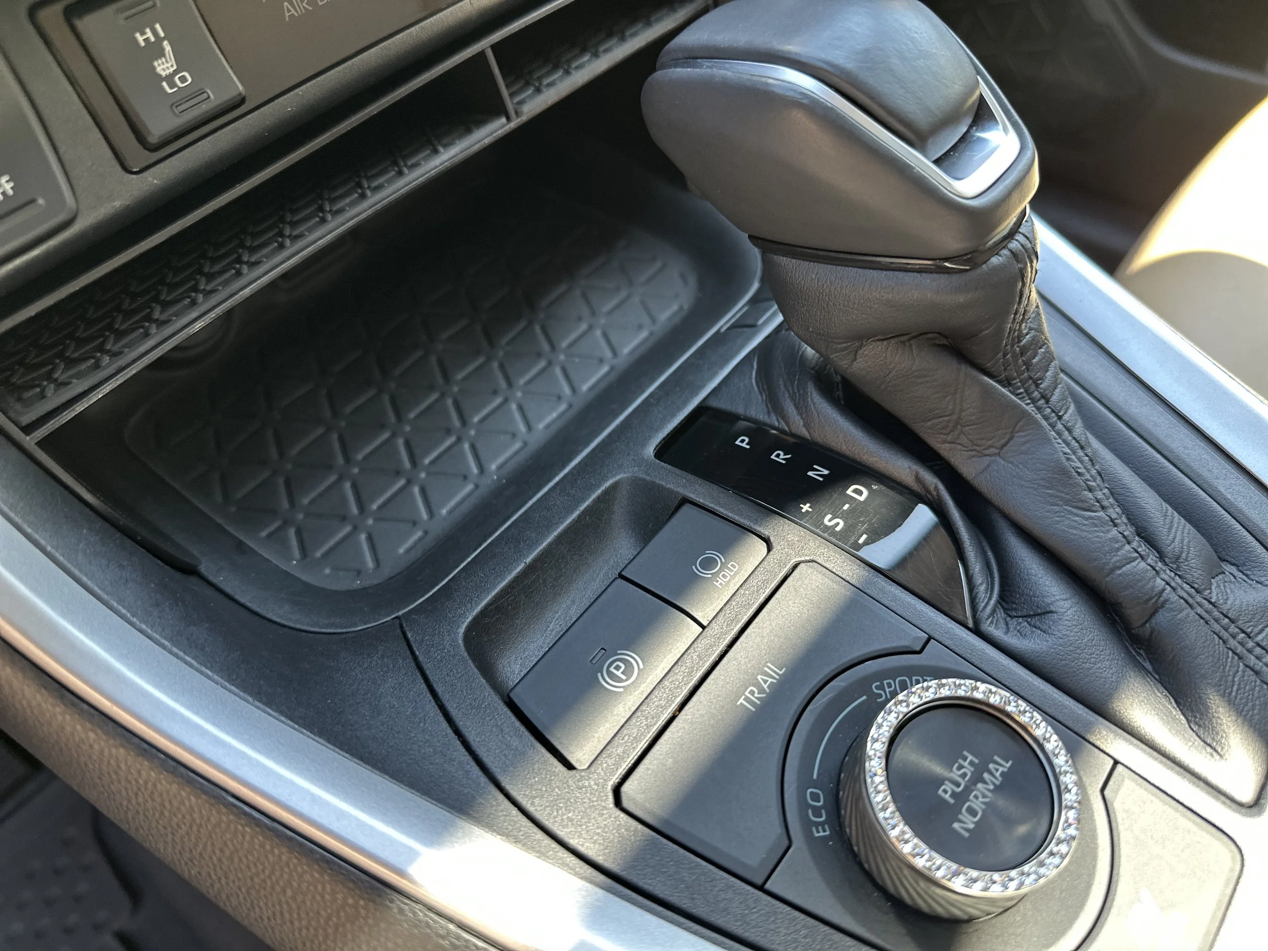 Center console of a vehicle featuring an automatic gear shift, electronic parking brake, and mode selector knob.