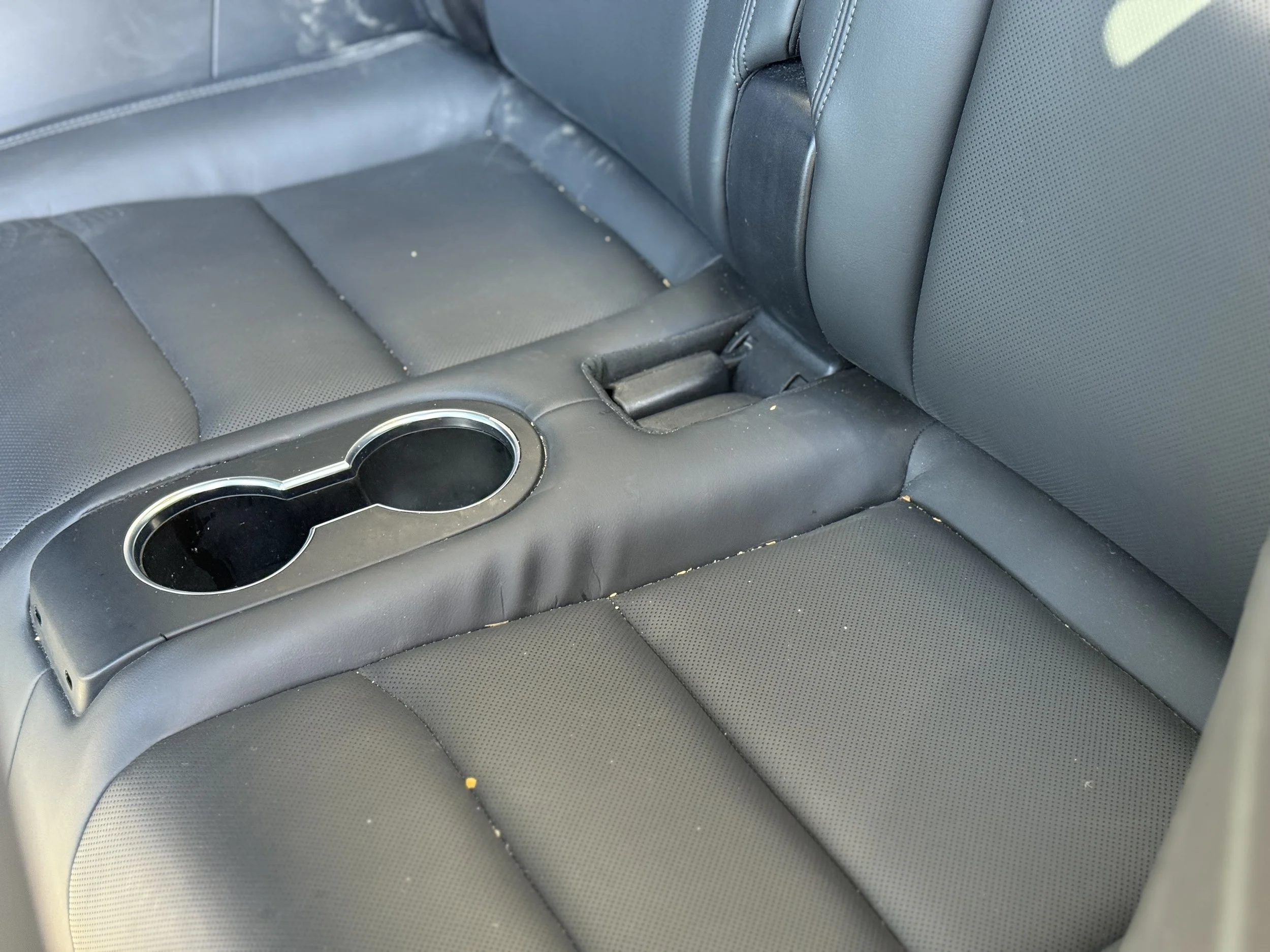 Close-up of a black car interior seat with a center console and cup holders, showing some dirt and minor wear.