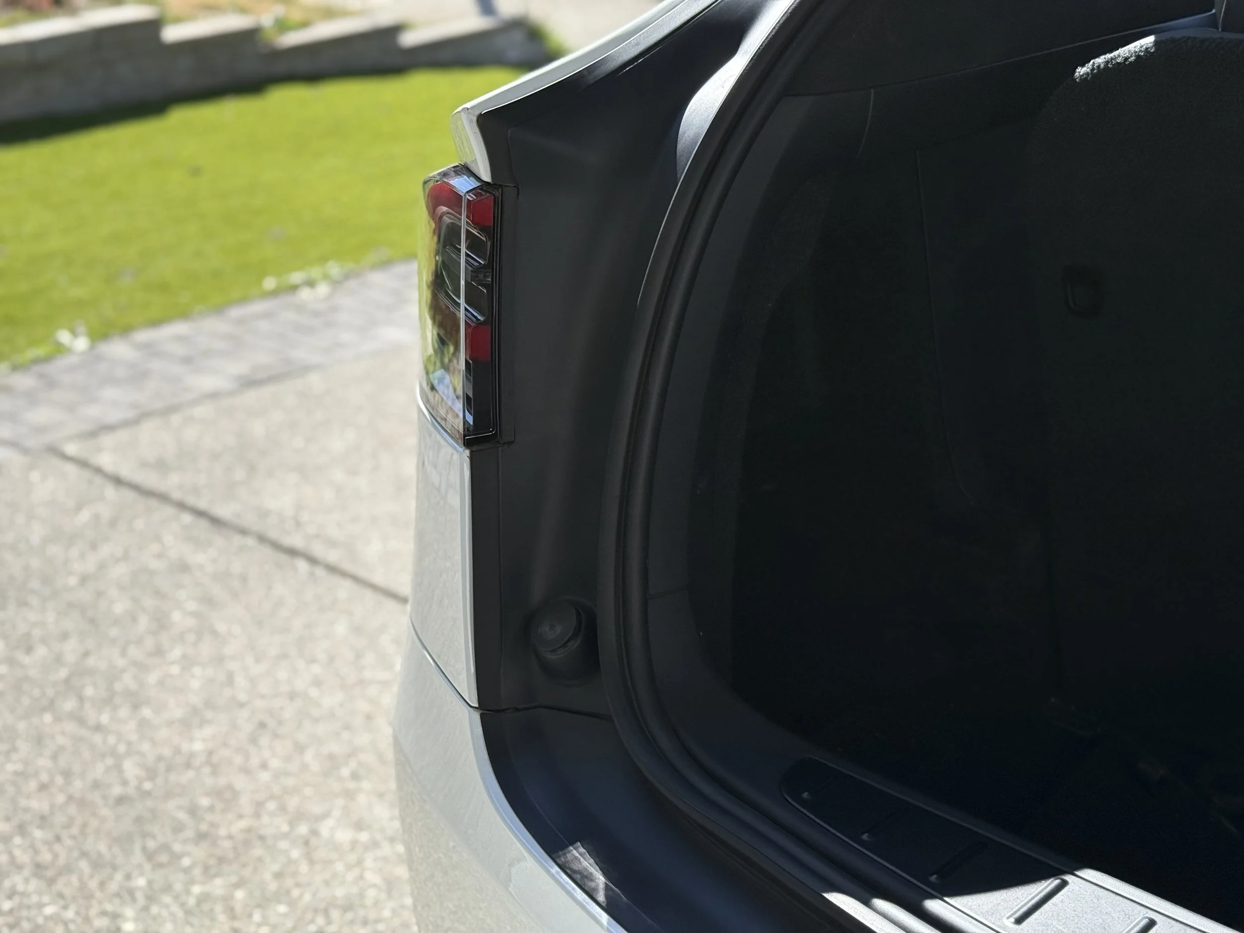 Open car trunk showing the interior and the rear tail light on an outdoor driveway.