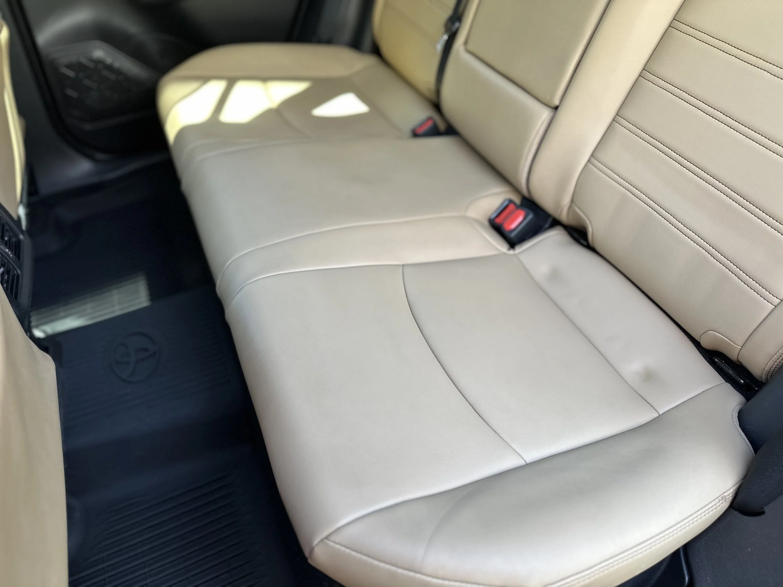 Front beige leather car seats with seat belts inside a vehicle.