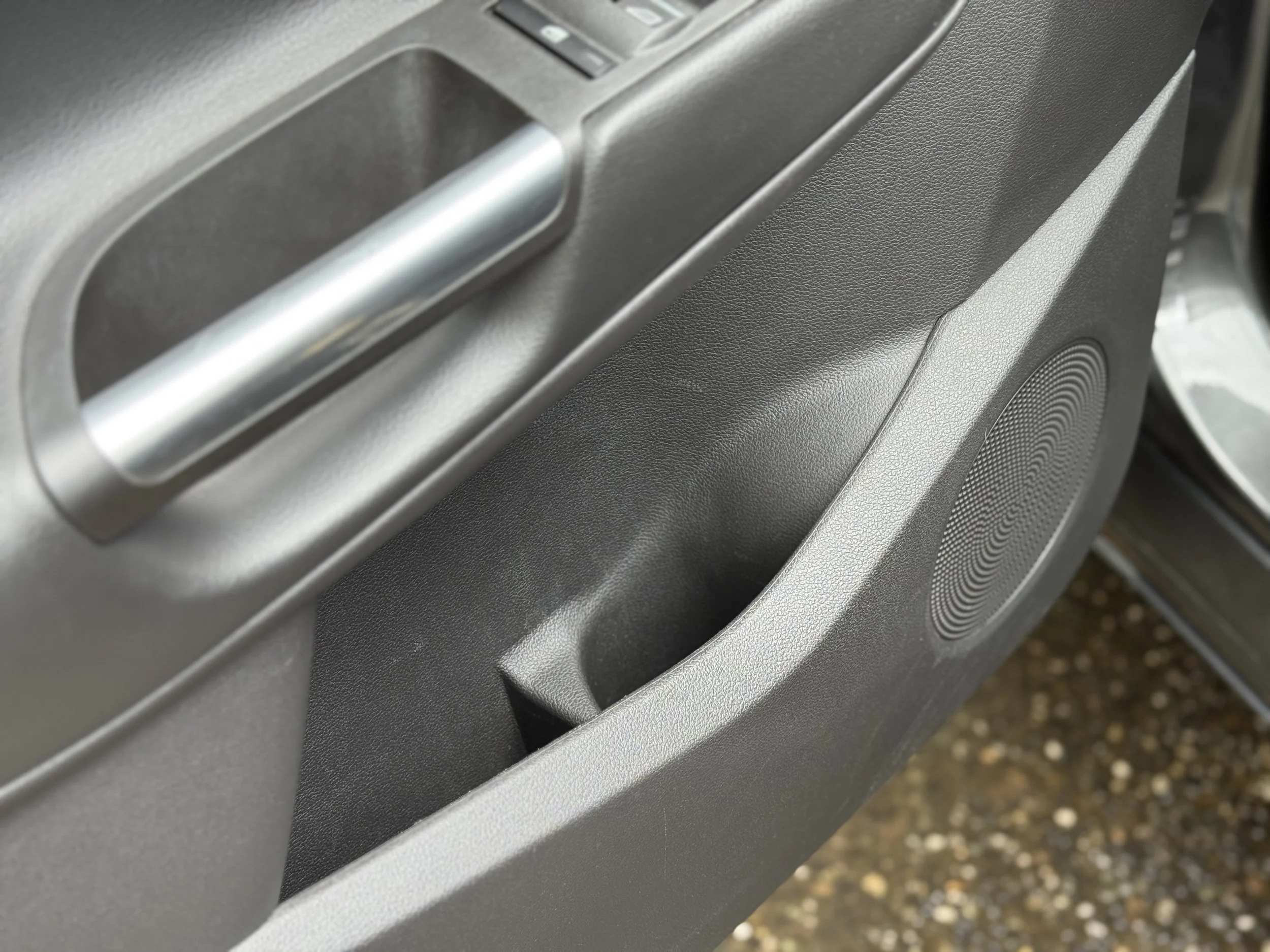 Close-up of a car door interior showing a handle, speaker, and storage compartment.
