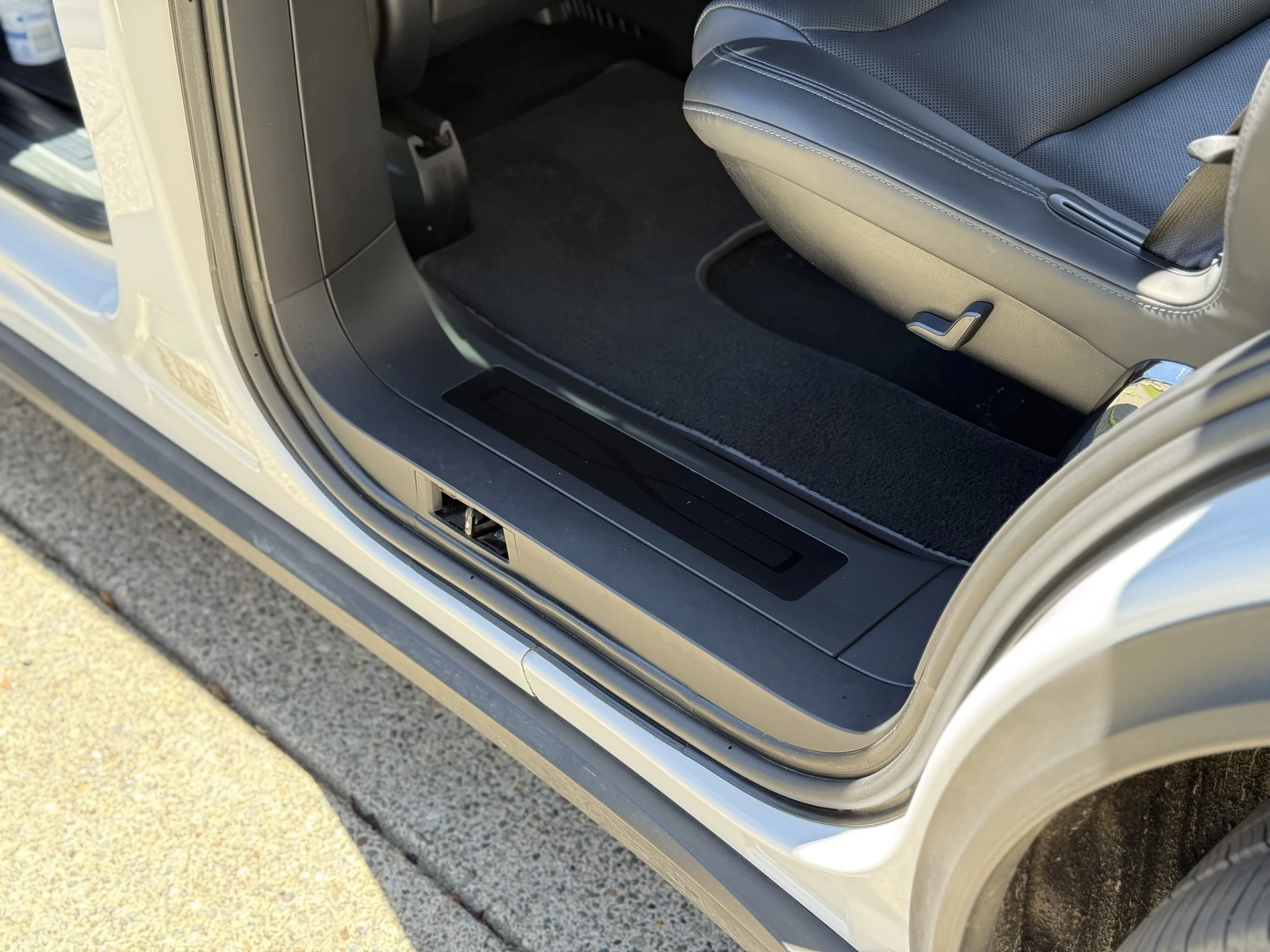 Open car door showing the car's interior with a black carpeted floor and a gray seat with a black seatbelt.