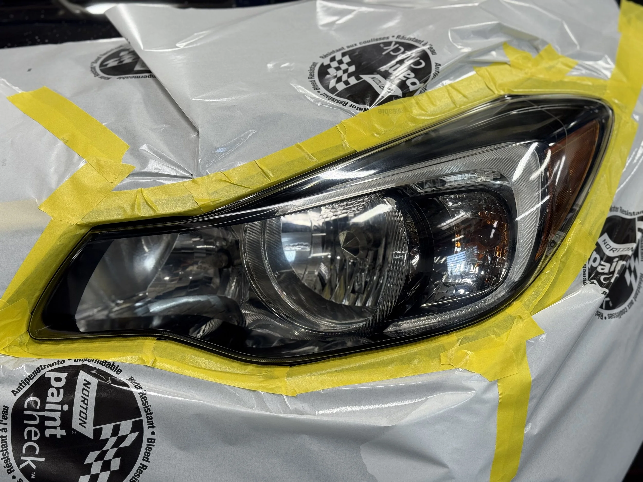 Close-up of a car headlight with masking tape and protective paper around it.