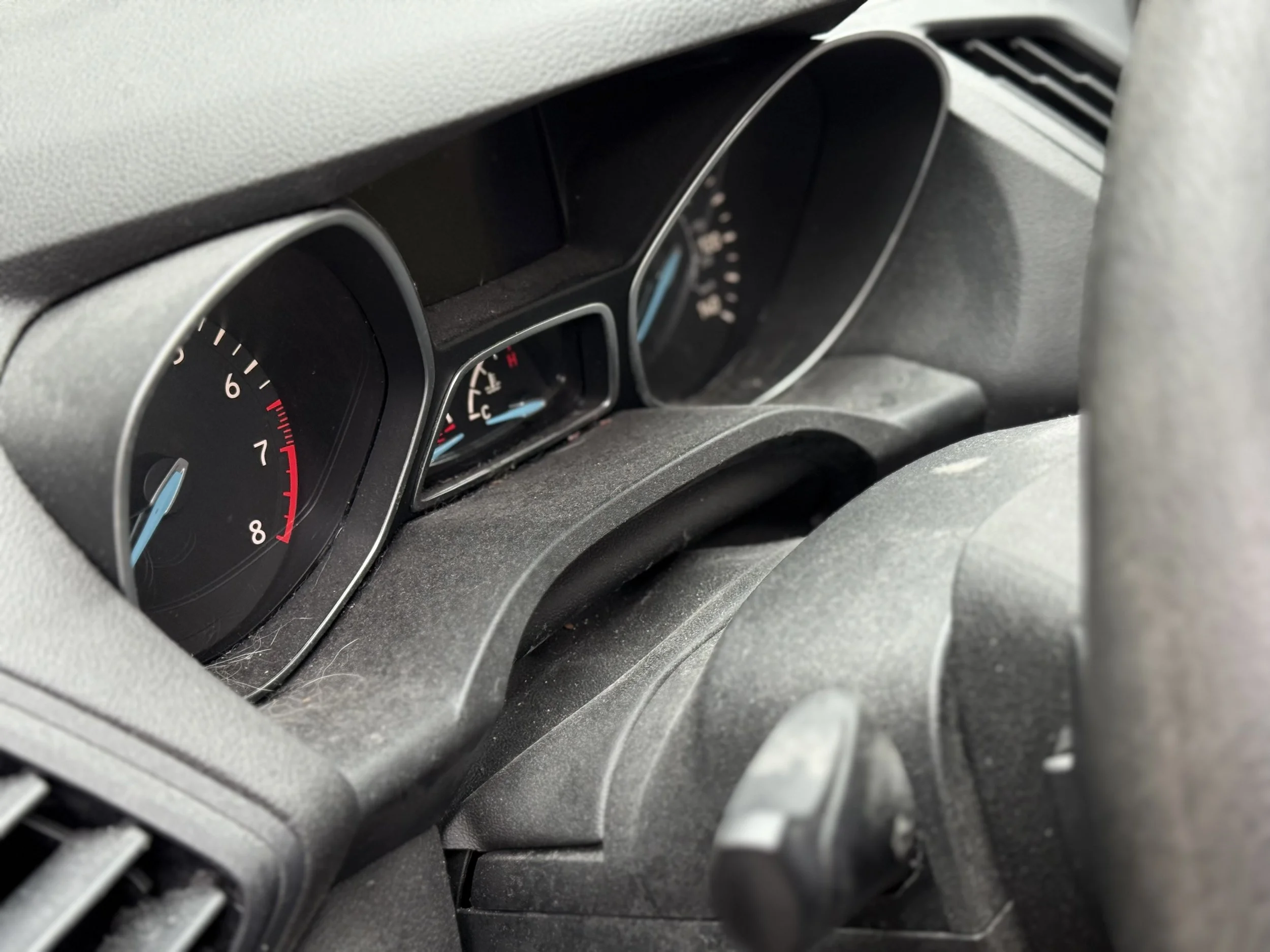 Close-up of a car dashboard showing the speedometer, fuel gauge, and other gauges, with a black interior and a steering wheel partially visible.