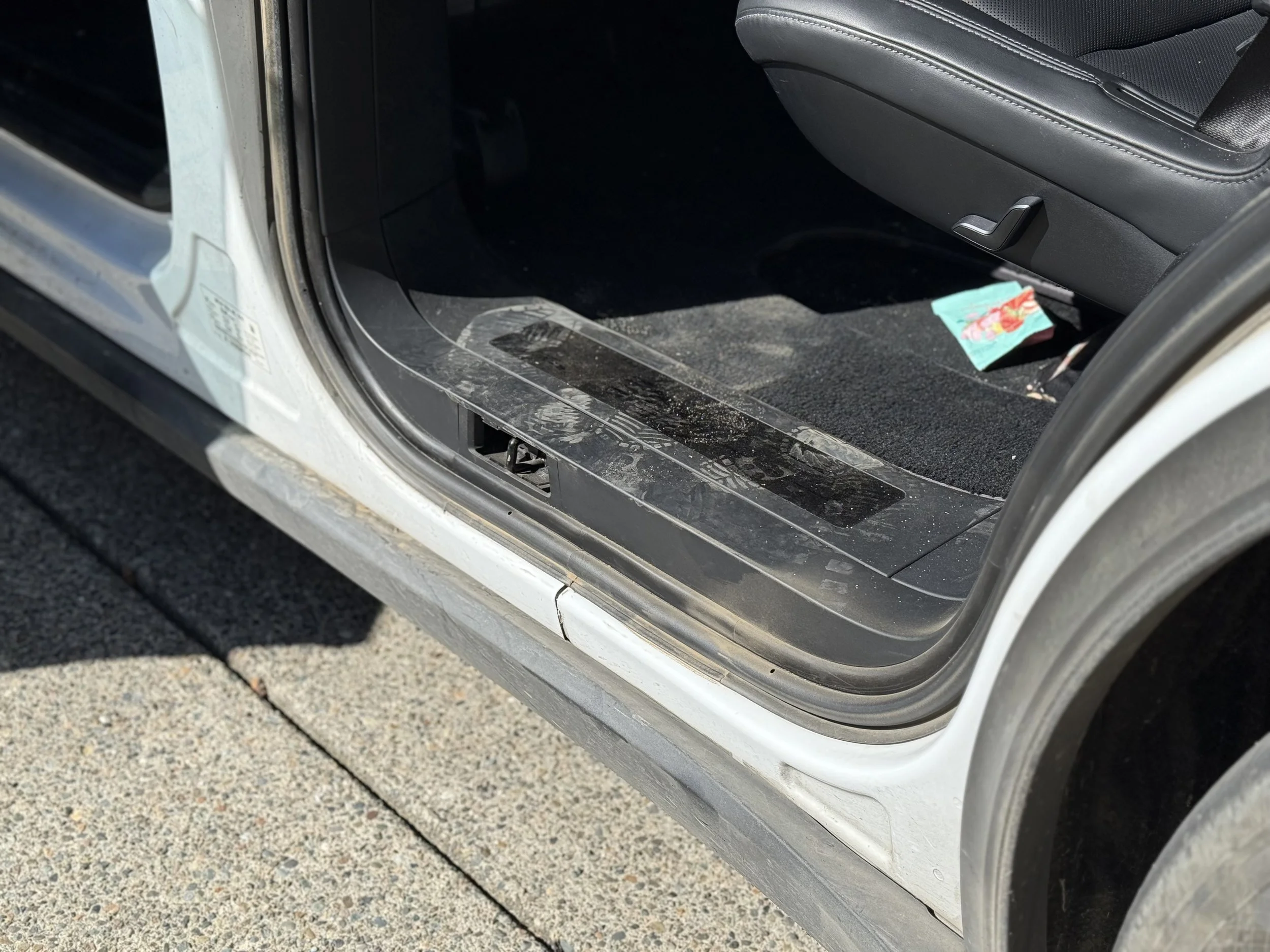 Close-up of the open passenger side door of a vehicle with dirty floor and a small packet of chips near the seat.