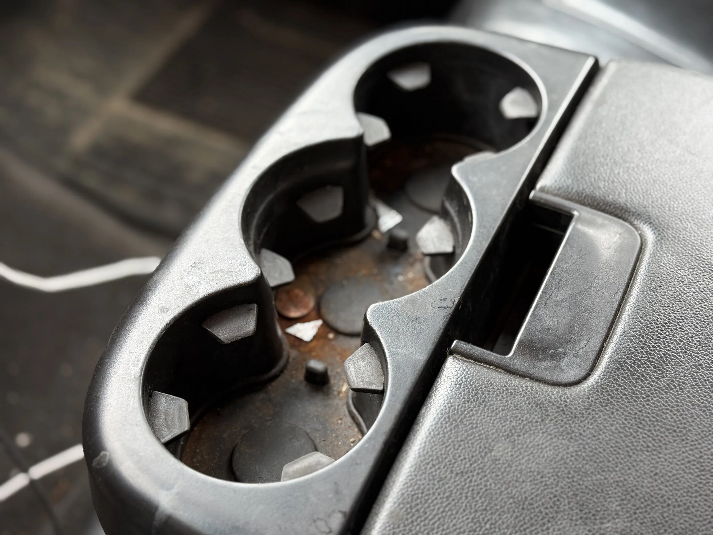 A close-up of a car's power outlet panel with three round sockets, some rust, and small debris inside.