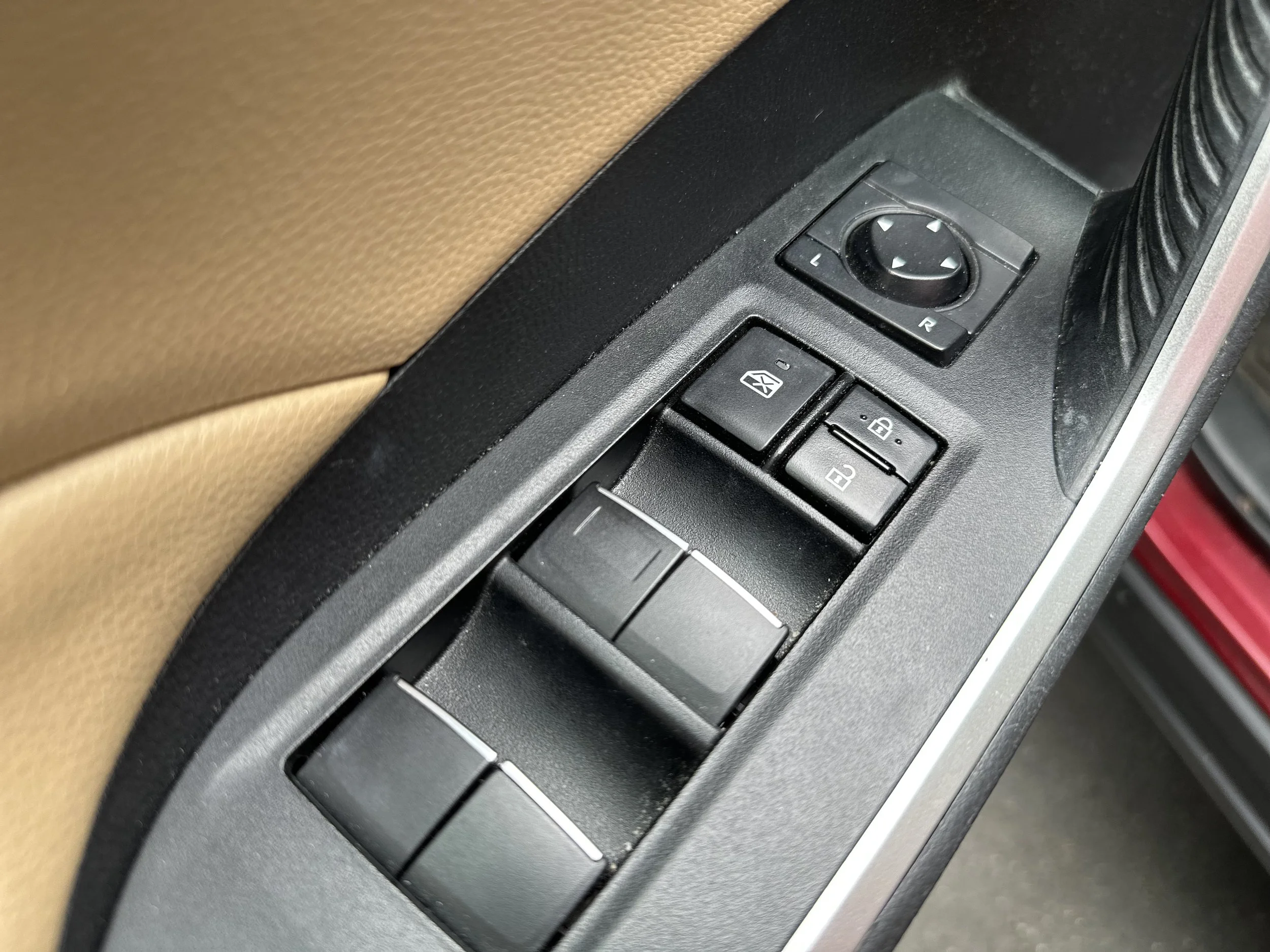Close-up of a car door's control panel with lock/unlock buttons, window switches, and side mirror adjustment joystick.