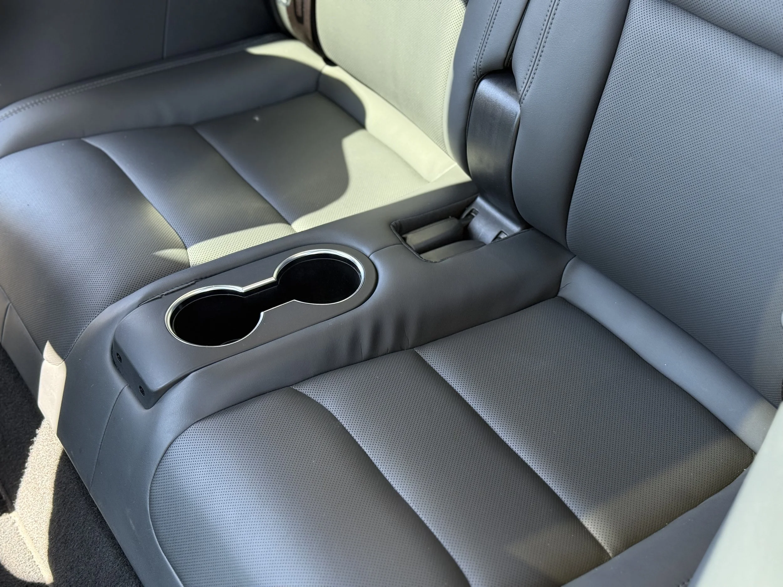 Backseat of a vehicle with gray leather upholstery, featuring a center armrest with two cup holders.