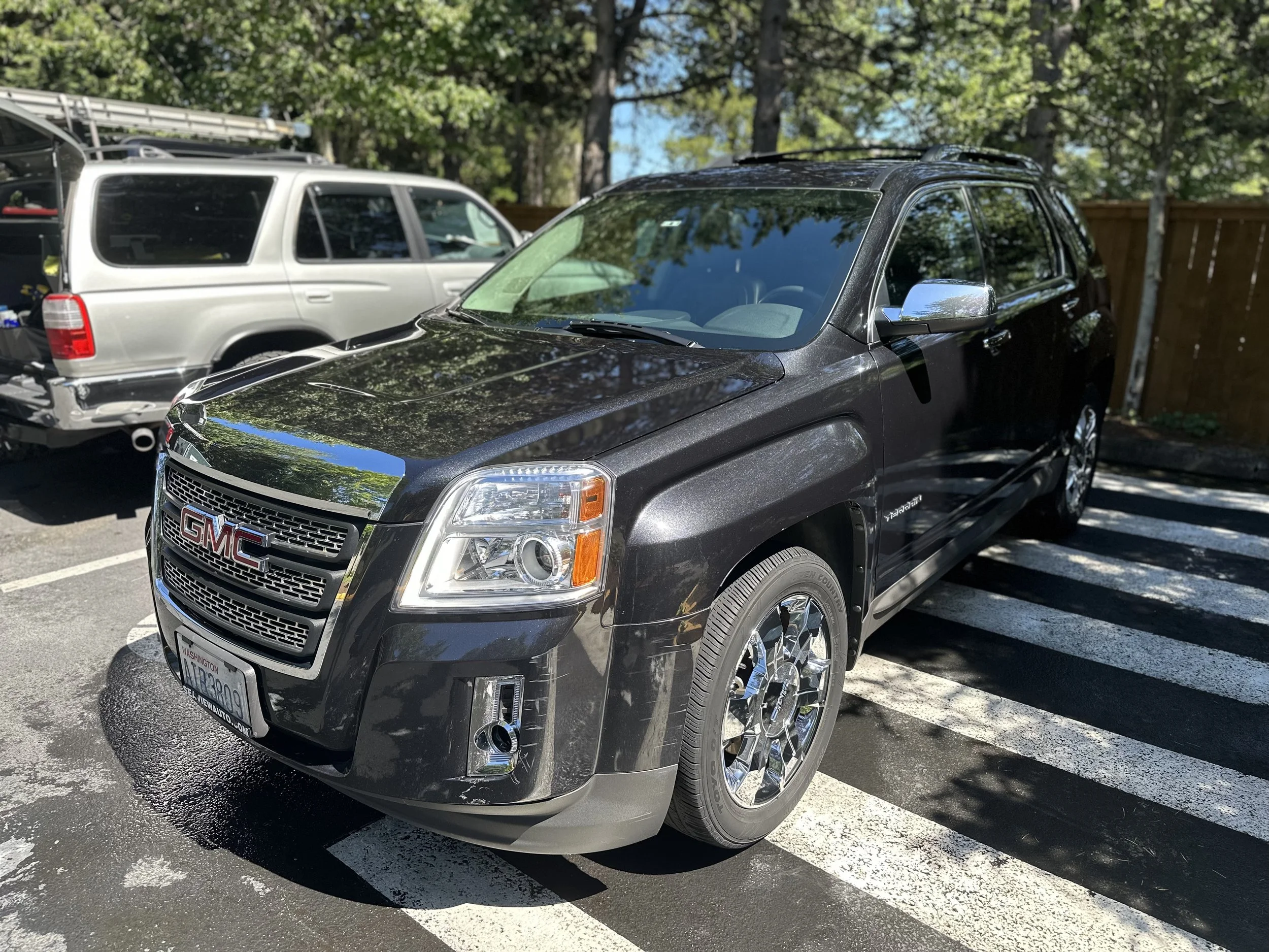 A black GMC SUV parked on a striped crosswalk with trees and a wooden fence in the background.