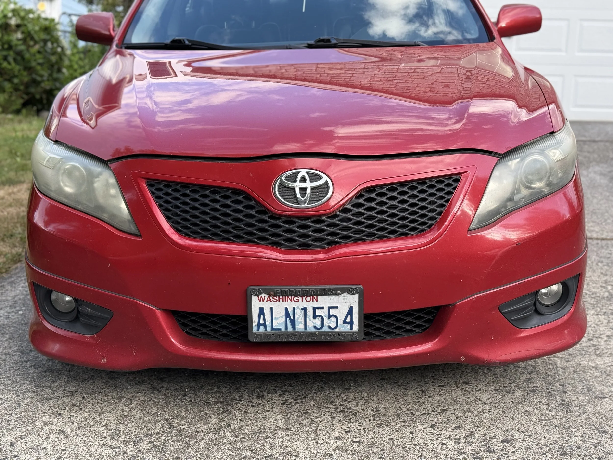 Front view of a red Toyota car with Washington license plate ALN1554 parked on a driveway, with a garage door in the background.