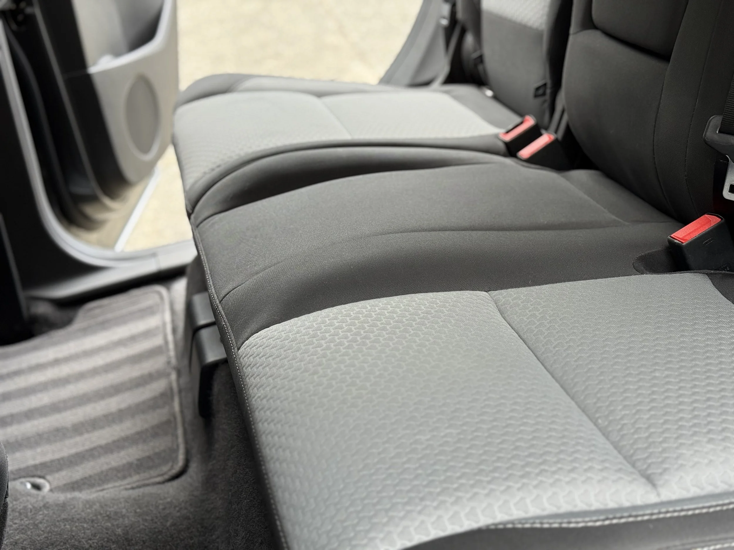 Rear seats of a vehicle with gray and black fabric upholstery and red seat belt latches.